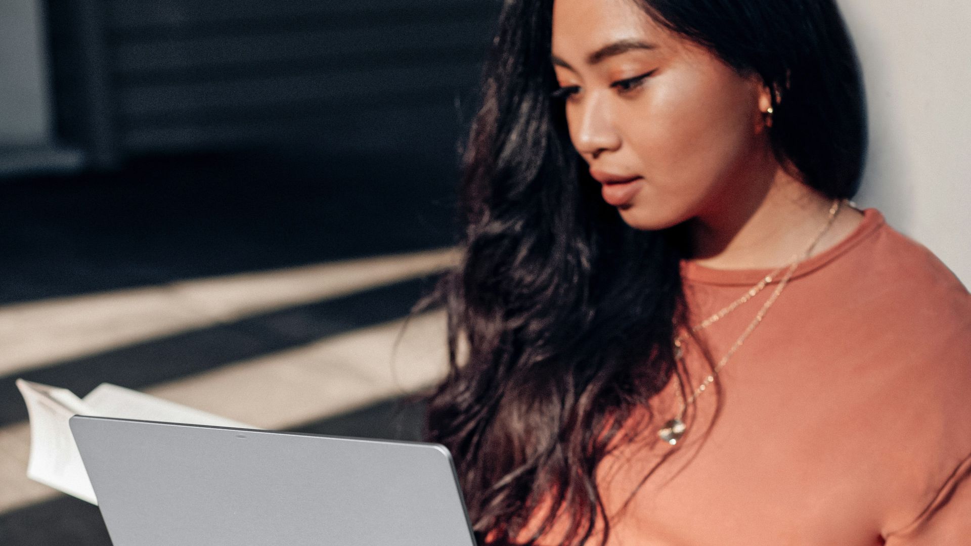 woman in orange long sleeve shirt and white pants sitting on floor using Surface Laptop