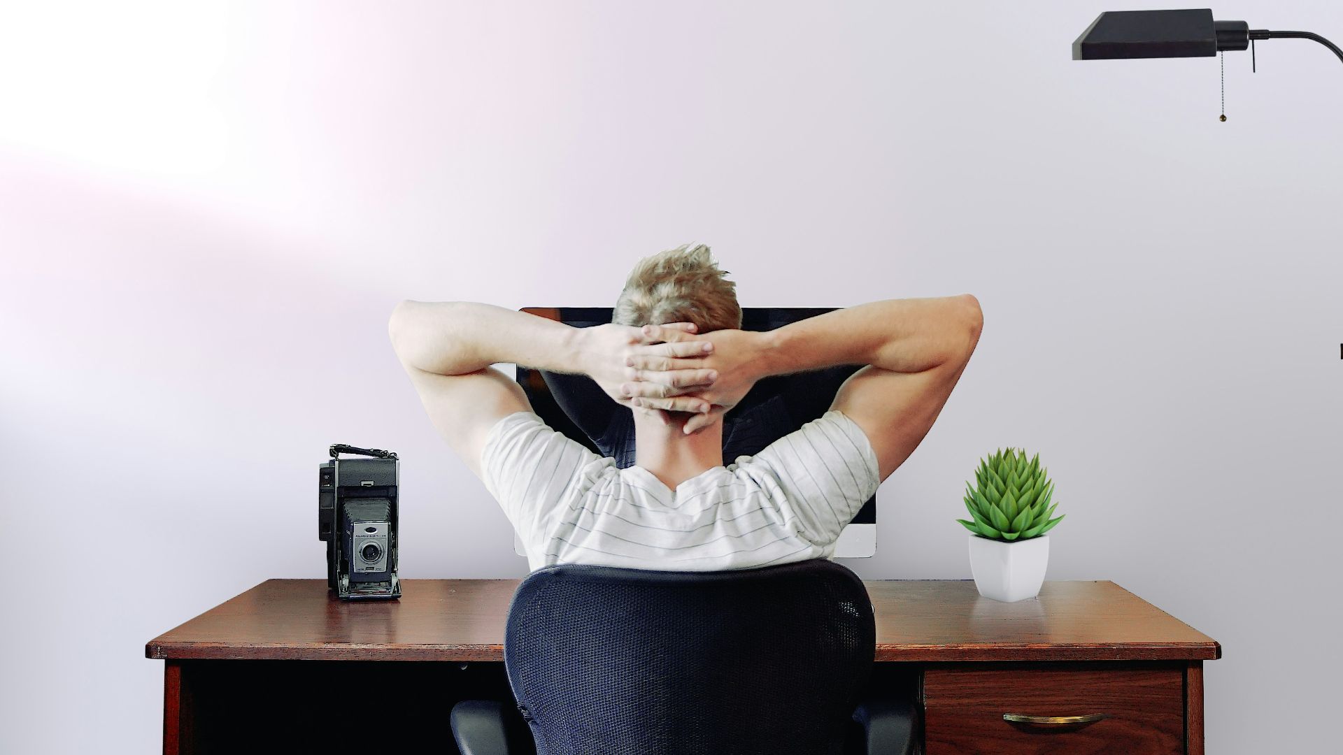 man holding his head while sitting on chair near computer desk