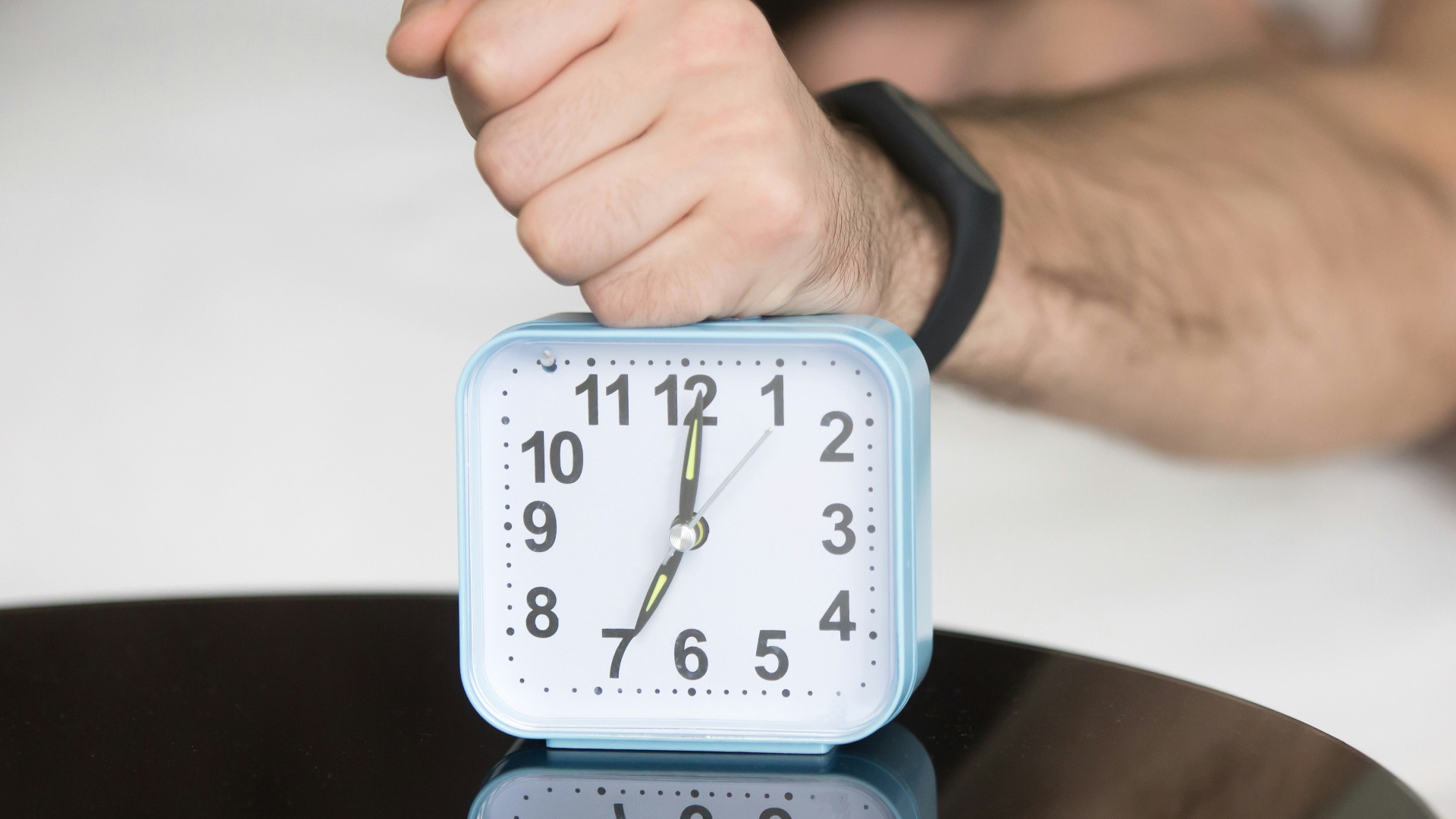 A man laying in bed with a clock on top of him
