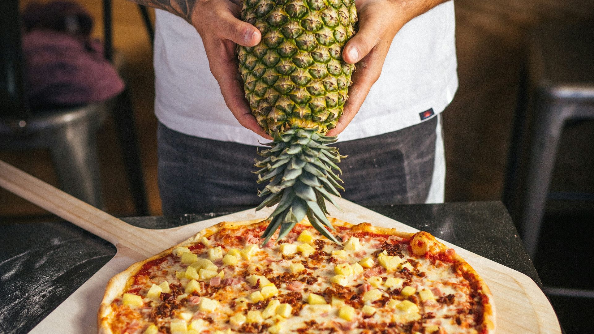 a man holding a pineapple on top of a pizza