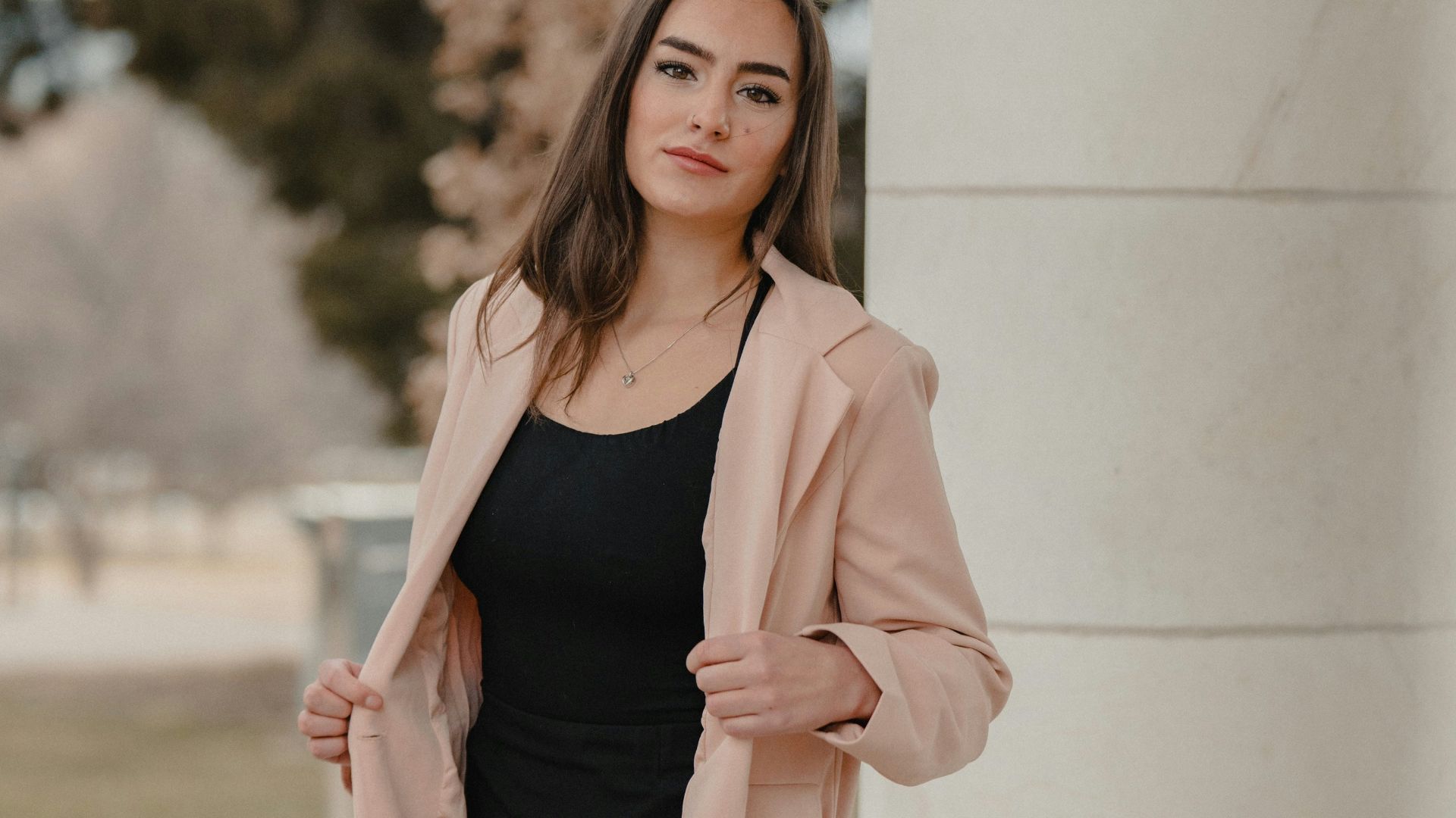 woman in pink blazer standing near white wall during daytime