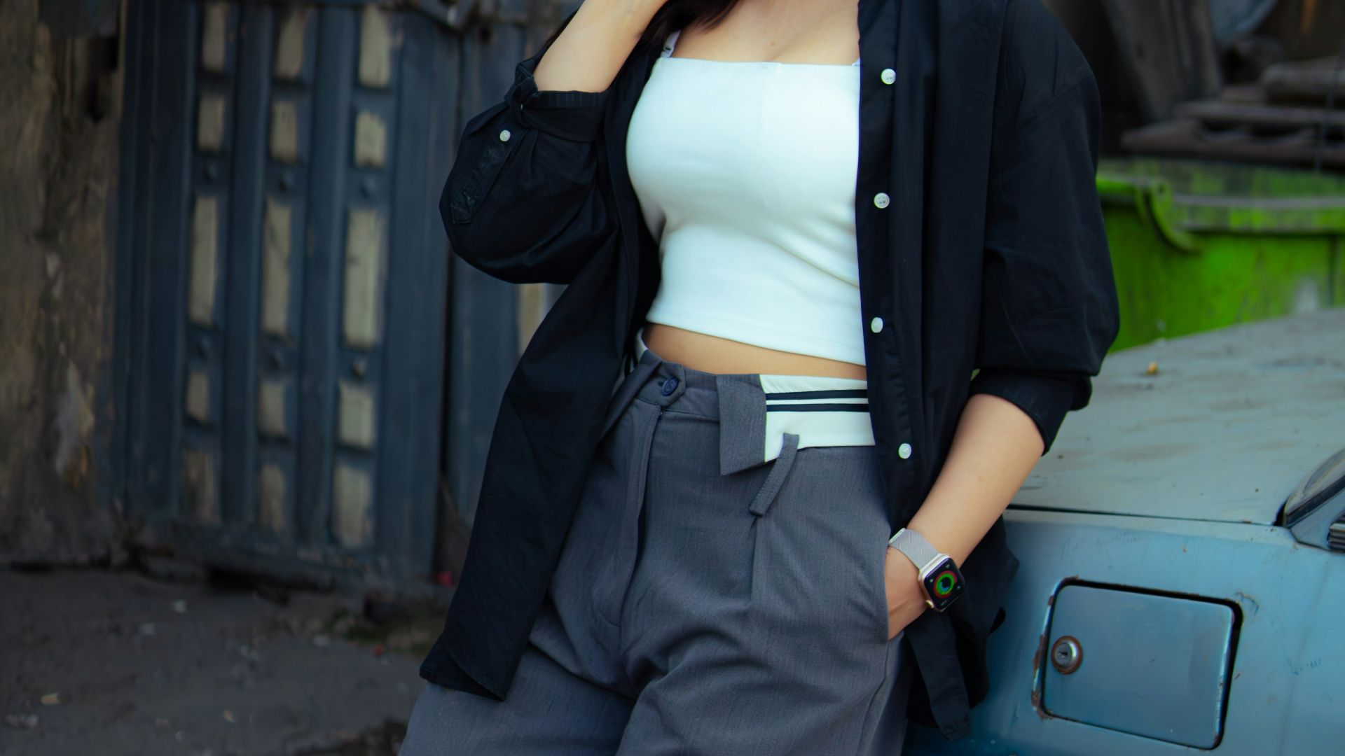A woman leans against a car in an urban setting.