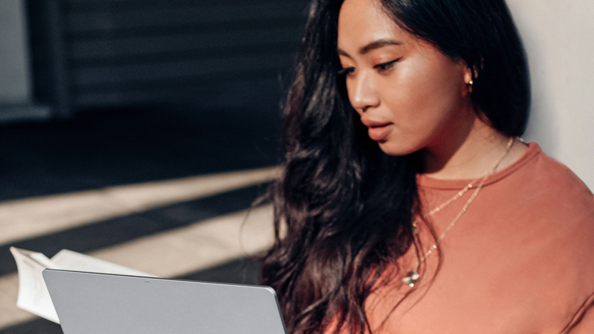 woman in orange long sleeve shirt and white pants sitting on floor using Surface Laptop