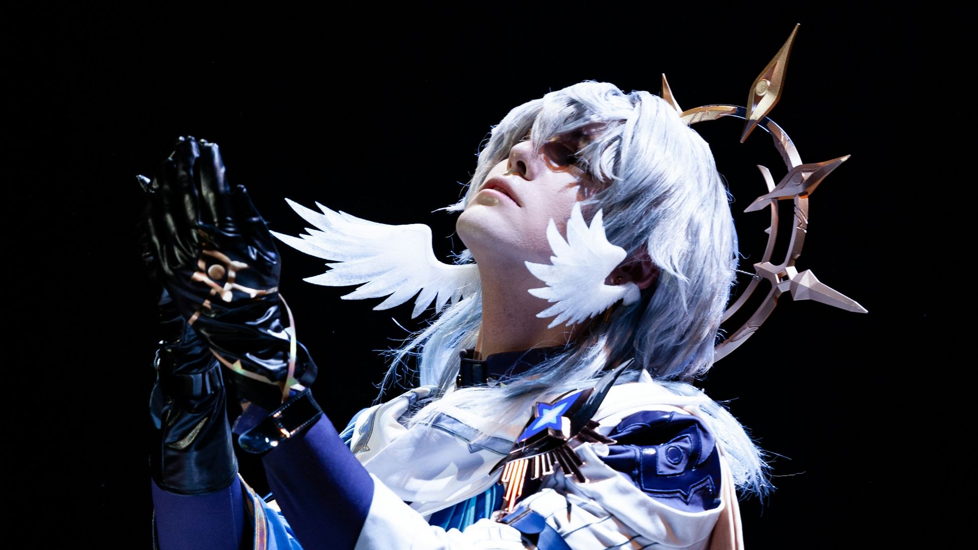 Cosplayer in white and blue costume with white wig praying.