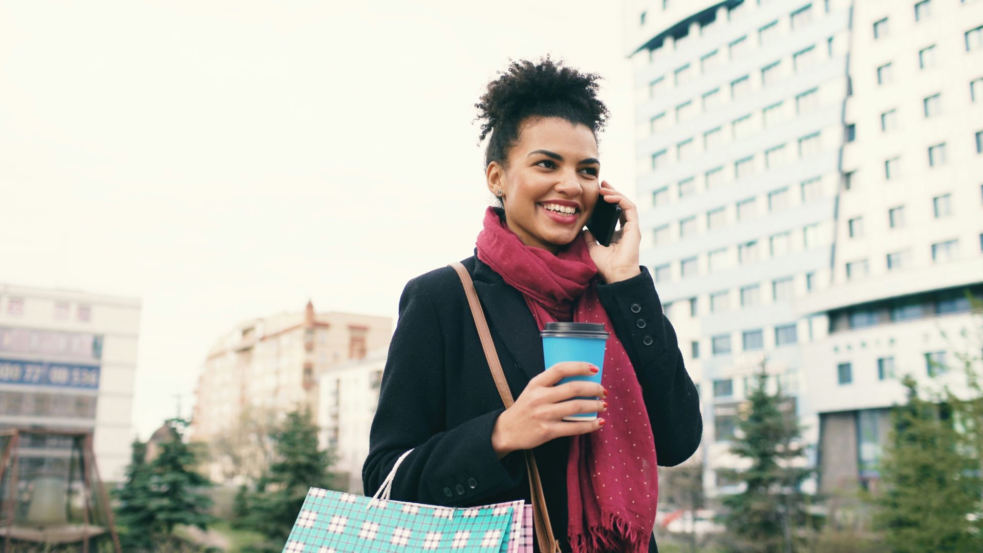 Woman talking on phone holding coffee and shopping bags