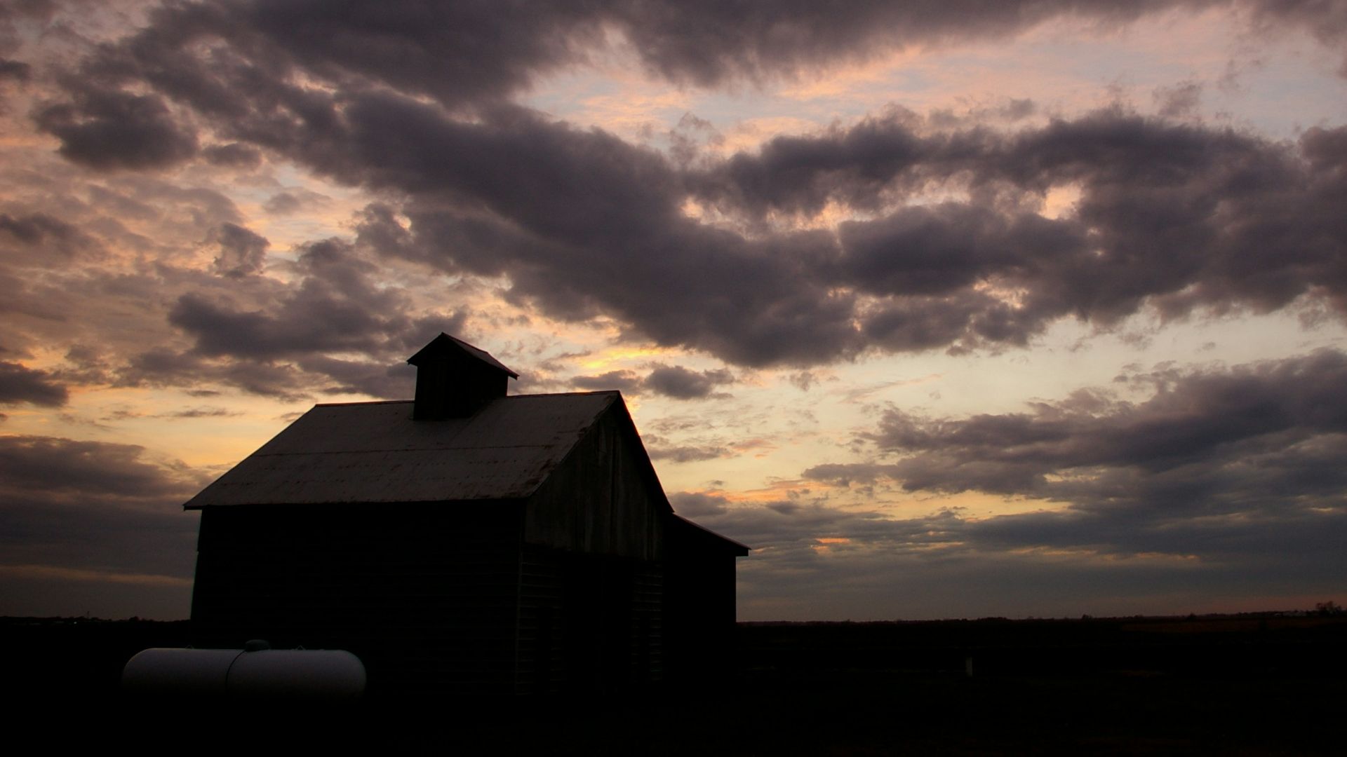a barn in a field with a cloudy sky in the background