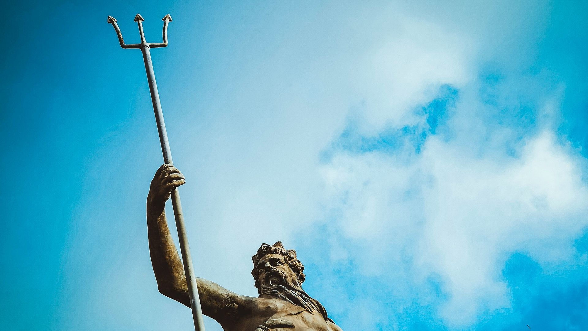 man holding trident statue under white clouds at daytime