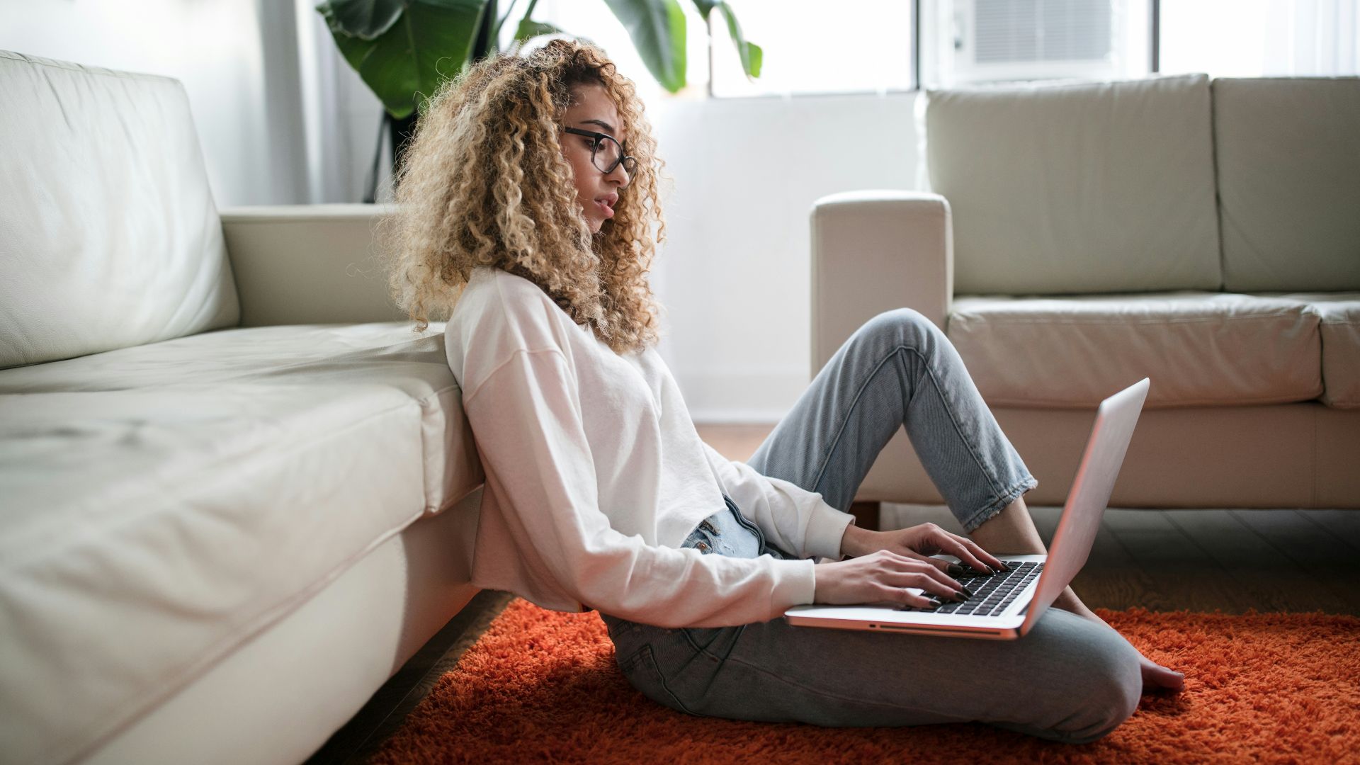 woman sitting on floor and leaning on couch using laptop
