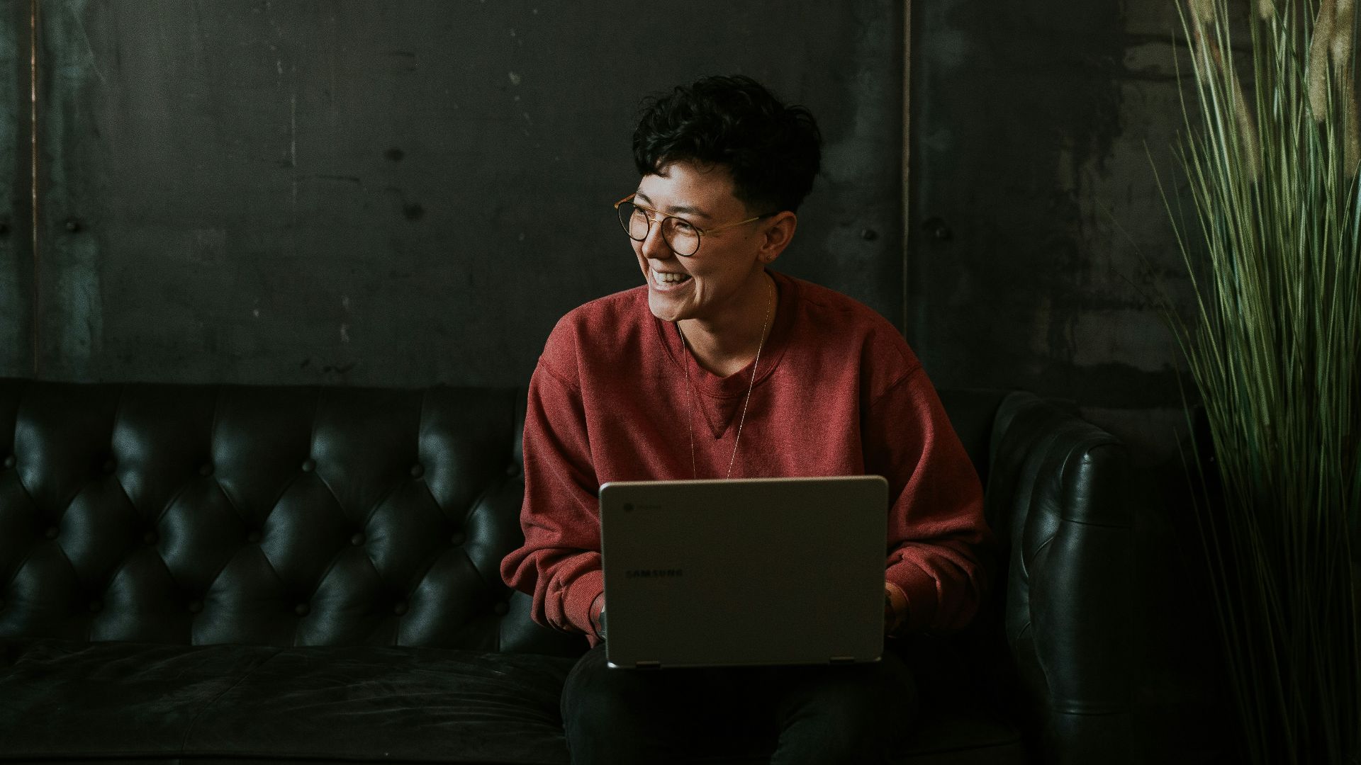 smiling man using laptop computer while sitting on black leather sofa