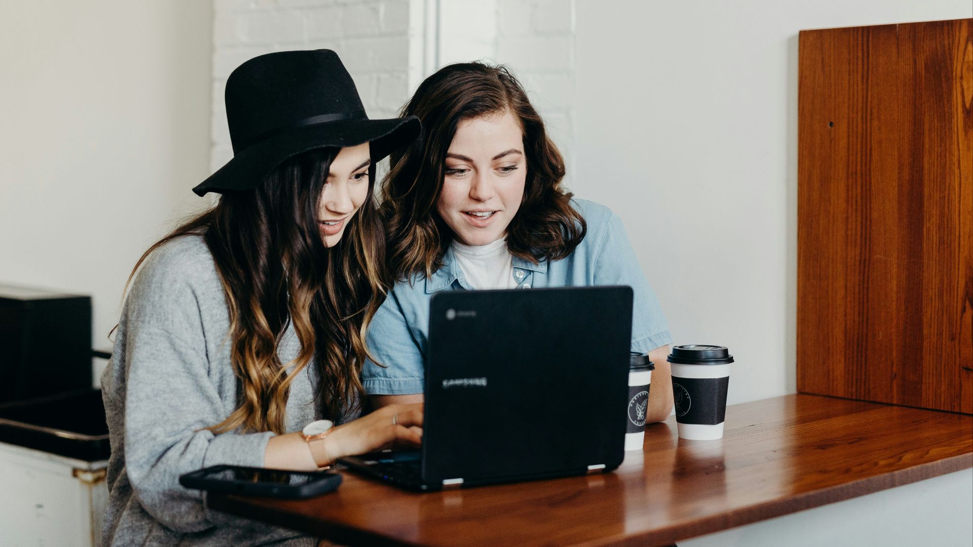 two woman sitting near table using Samsung laptop