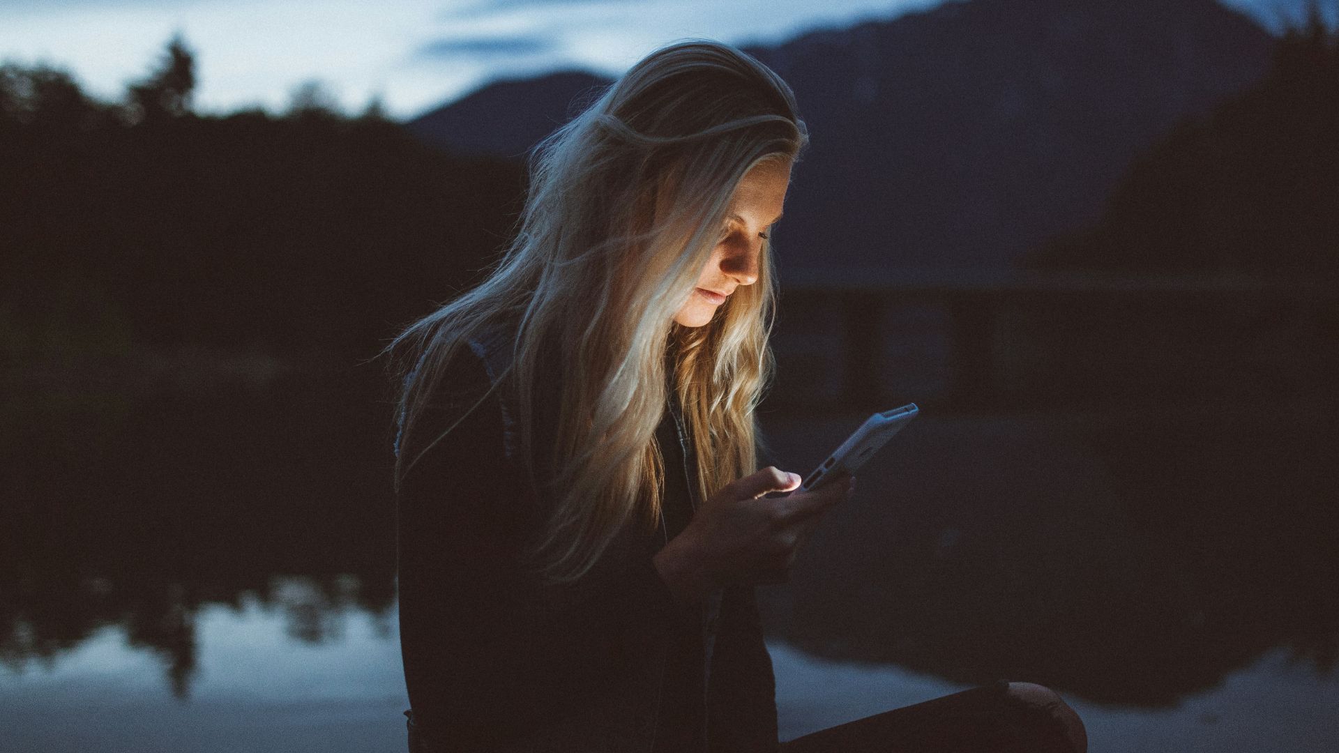 woman looking at phone beside body of water