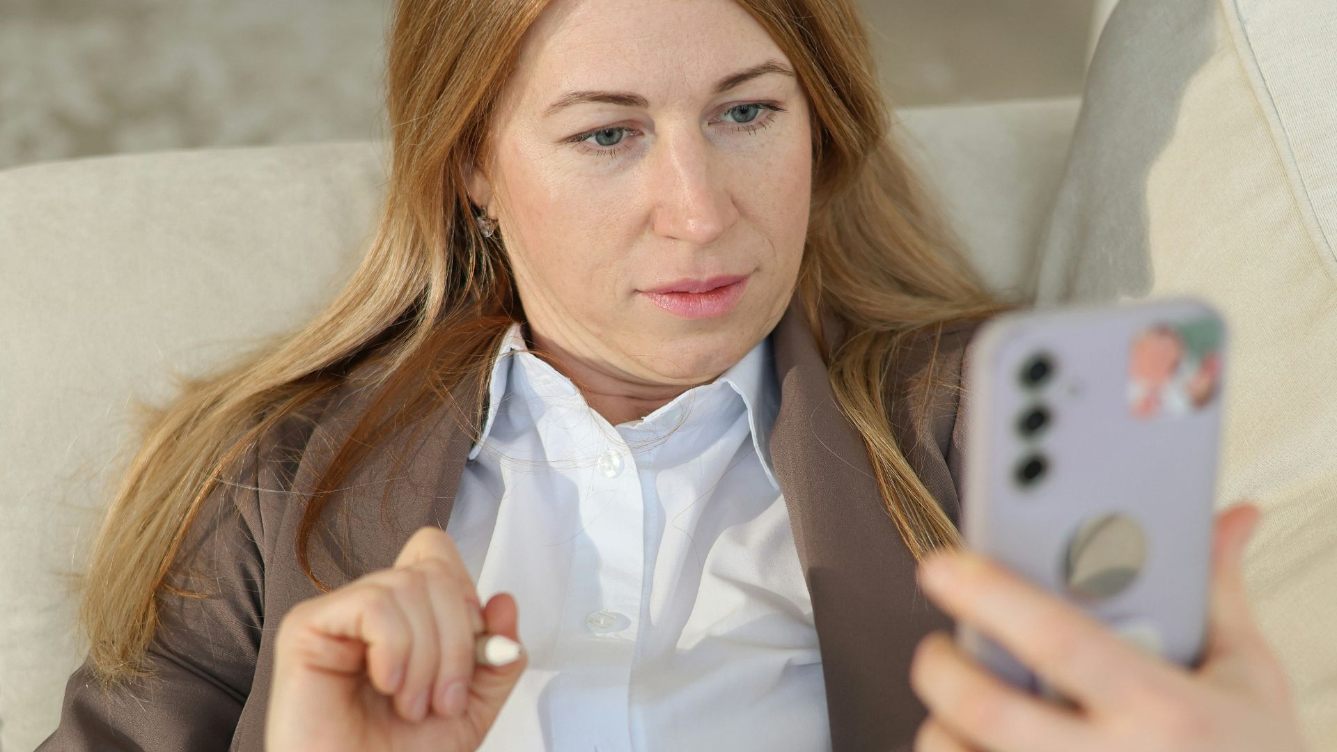 Woman looking at phone while holding a pen and notebook.