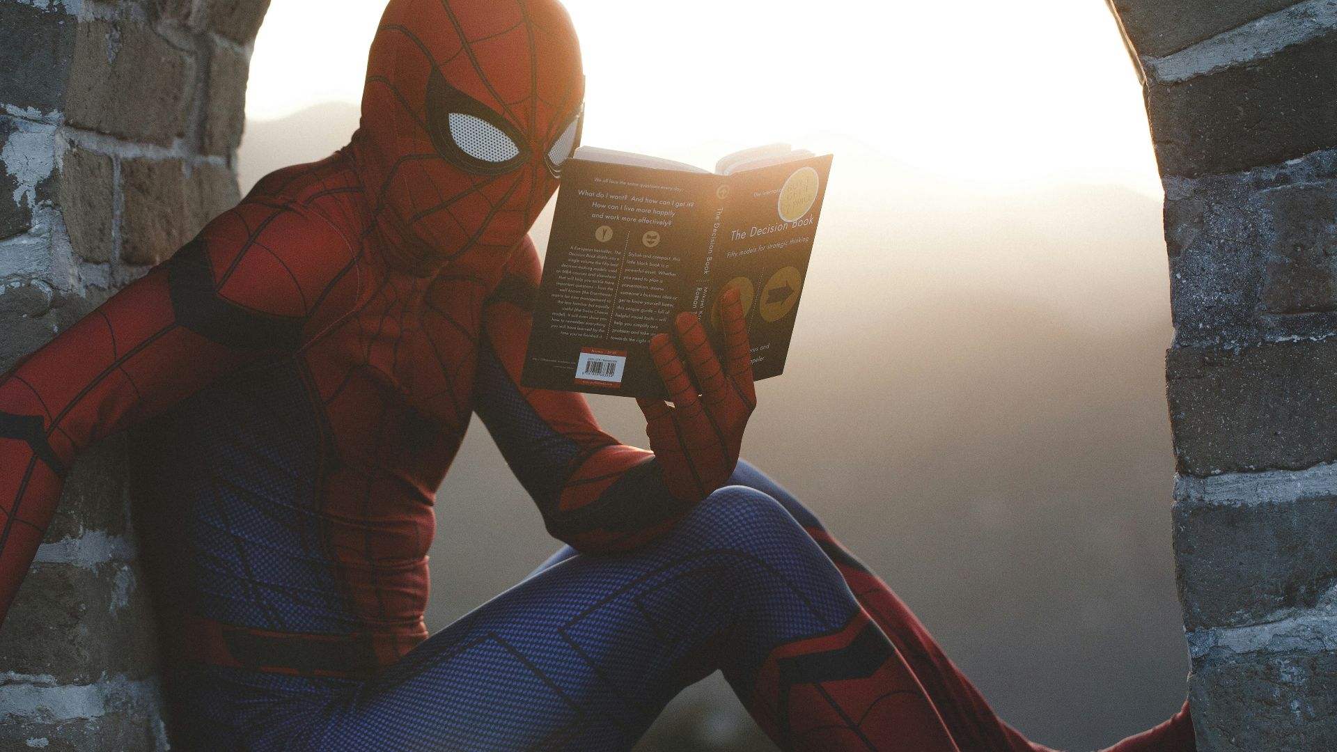 Spider-Man leaning on concrete brick while reading book