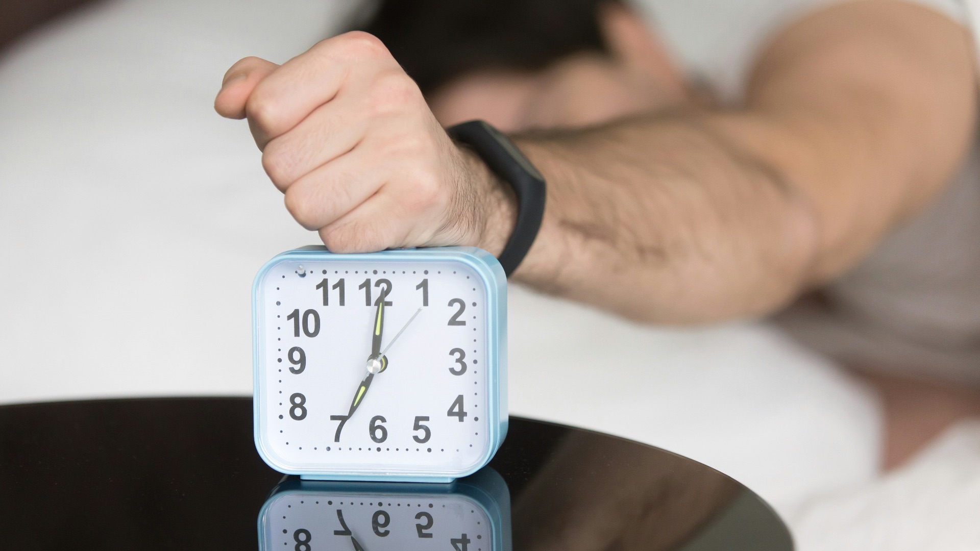 A man laying in bed with a clock on top of him