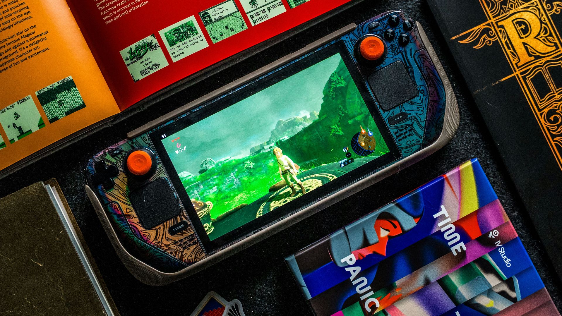 Gaming handheld, books, and phone on dark surface.