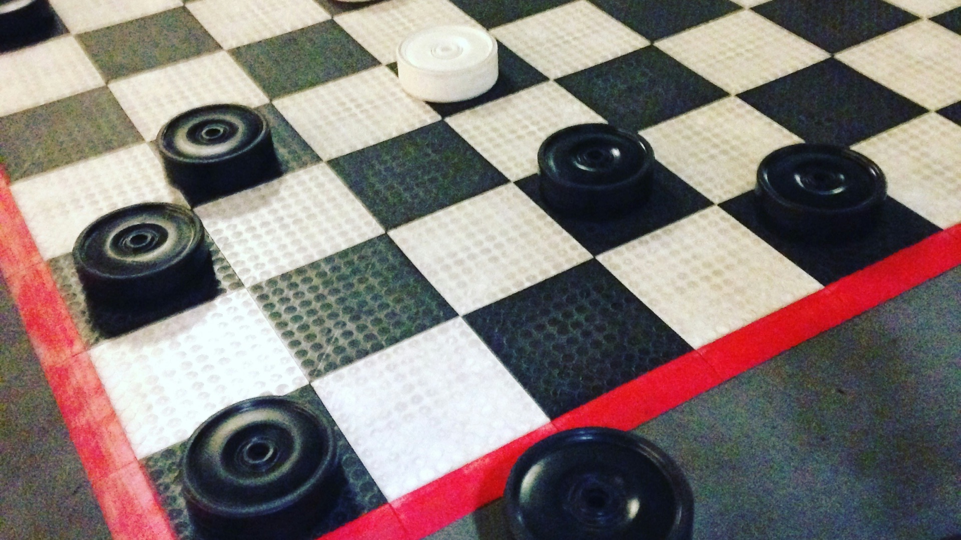 large black and white barbell game pieces on large white and black checked game board