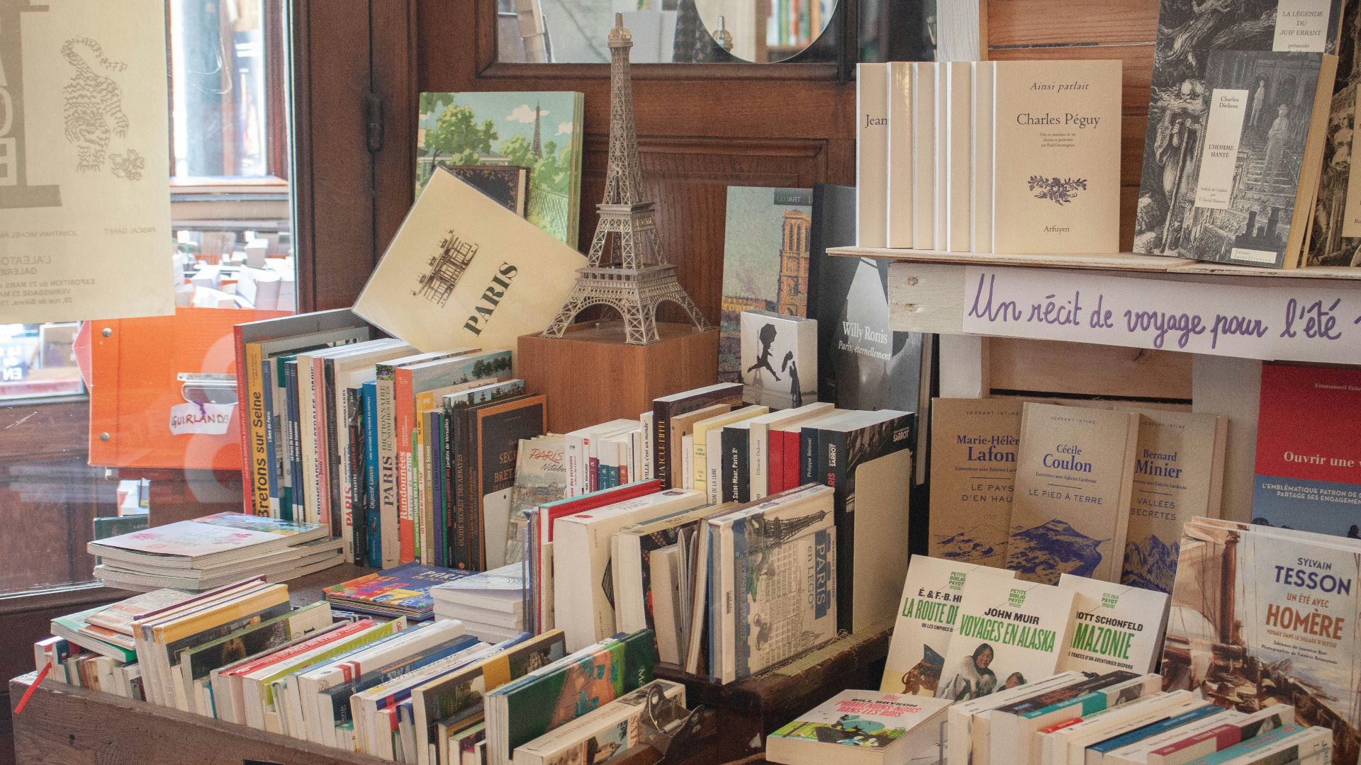 many books are stacked on a table in front of a window