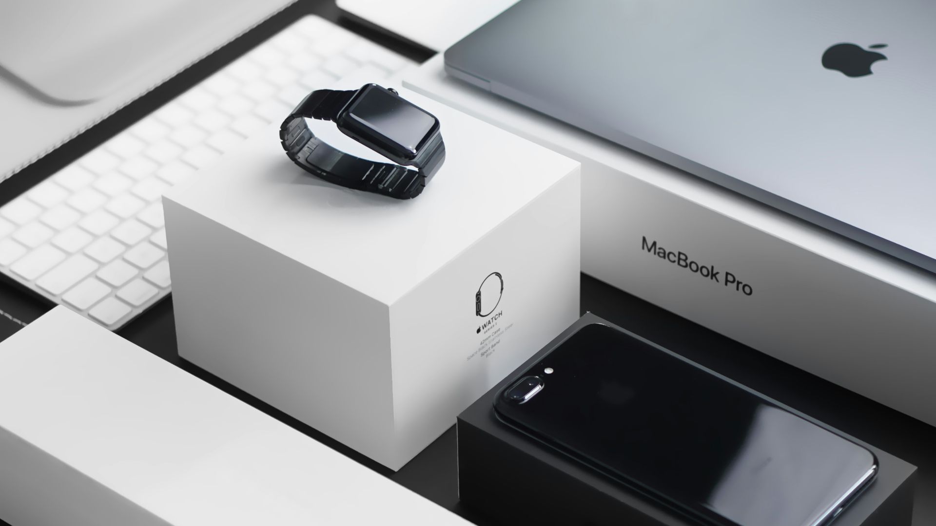 space black case Apple Watch, silver MacBook Pro, jet black iPhone 7 Plus, and silver iMac with corresponding boxes