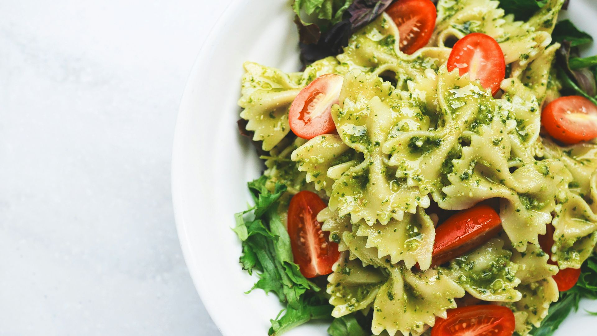 Pesto pasta with sliced tomatoes served on white ceramic plate