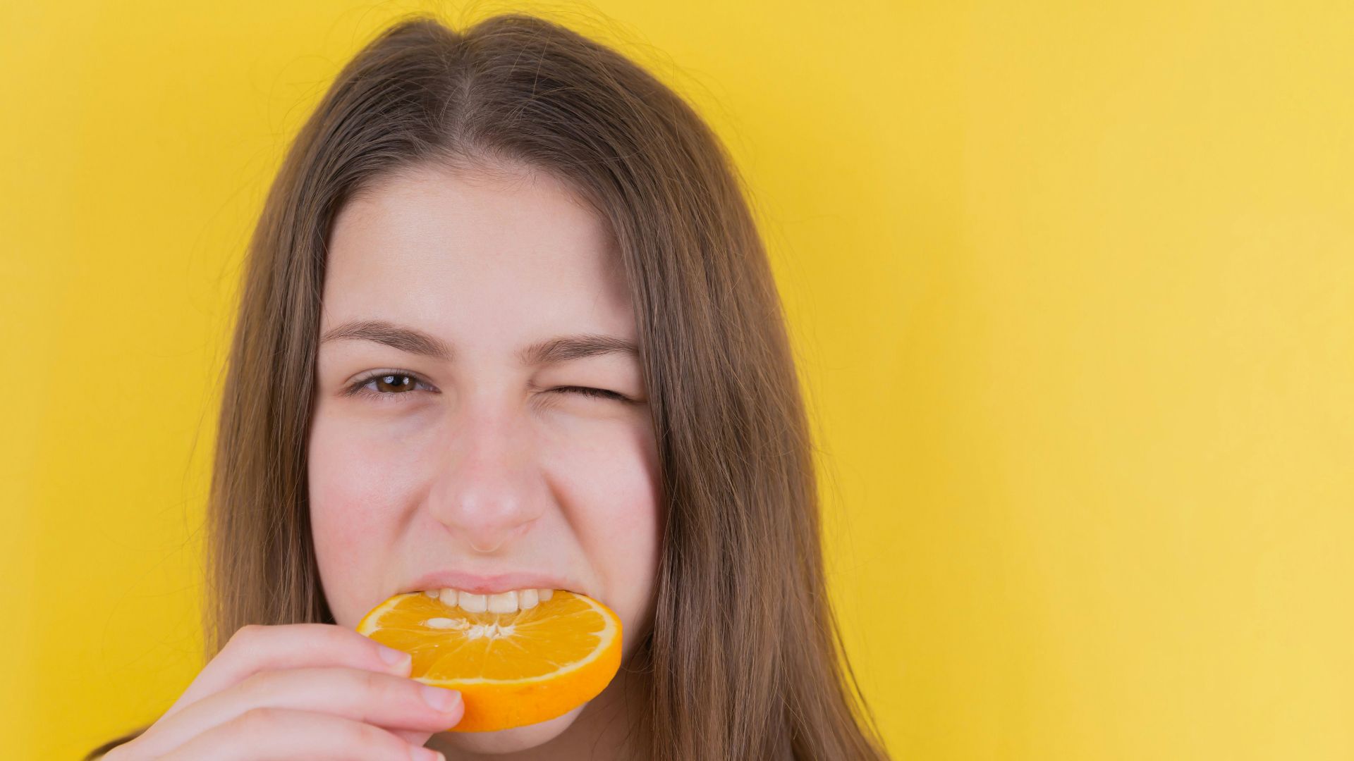 girl holding orange fruit in front of yellow wall