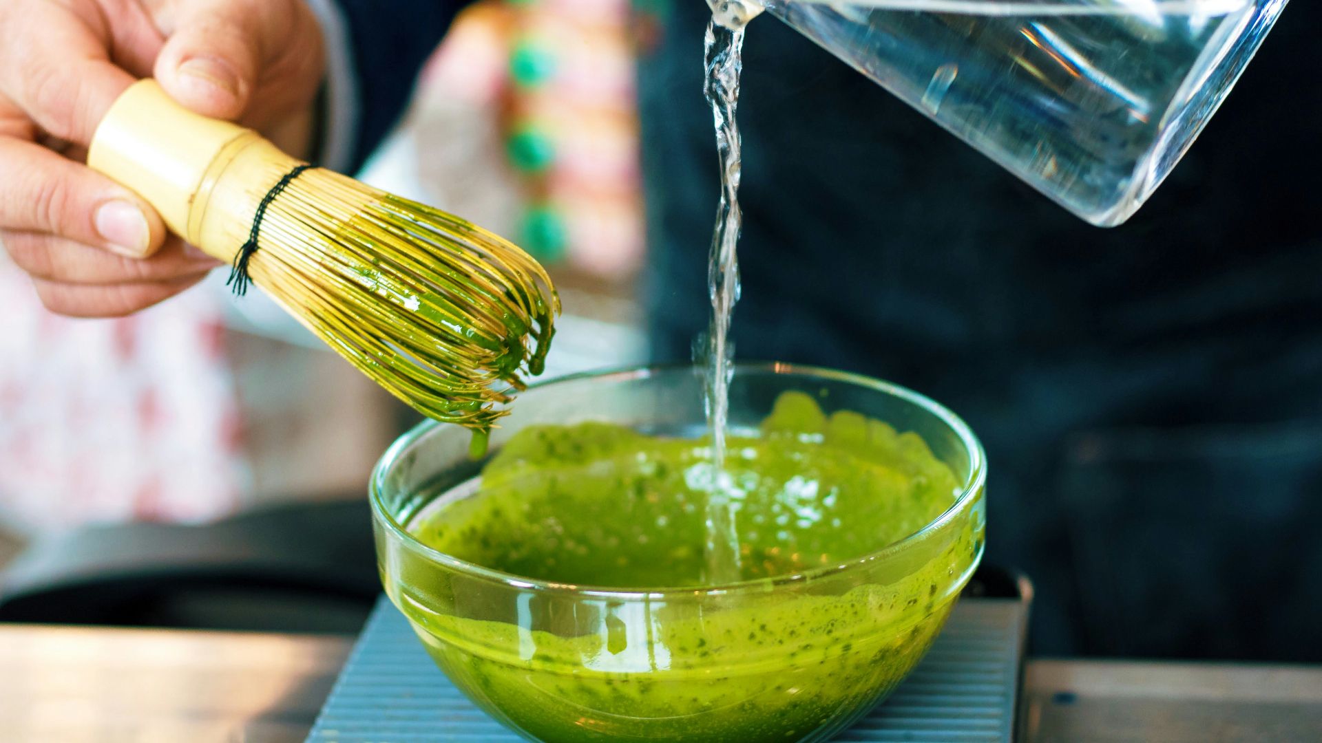 person pouring water into green sauce