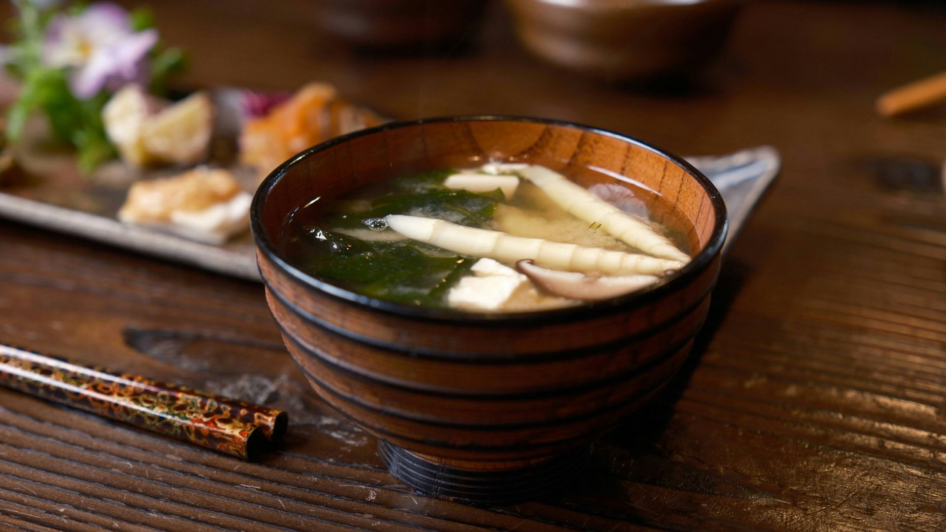 a wooden bowl filled with soup next to chopsticks