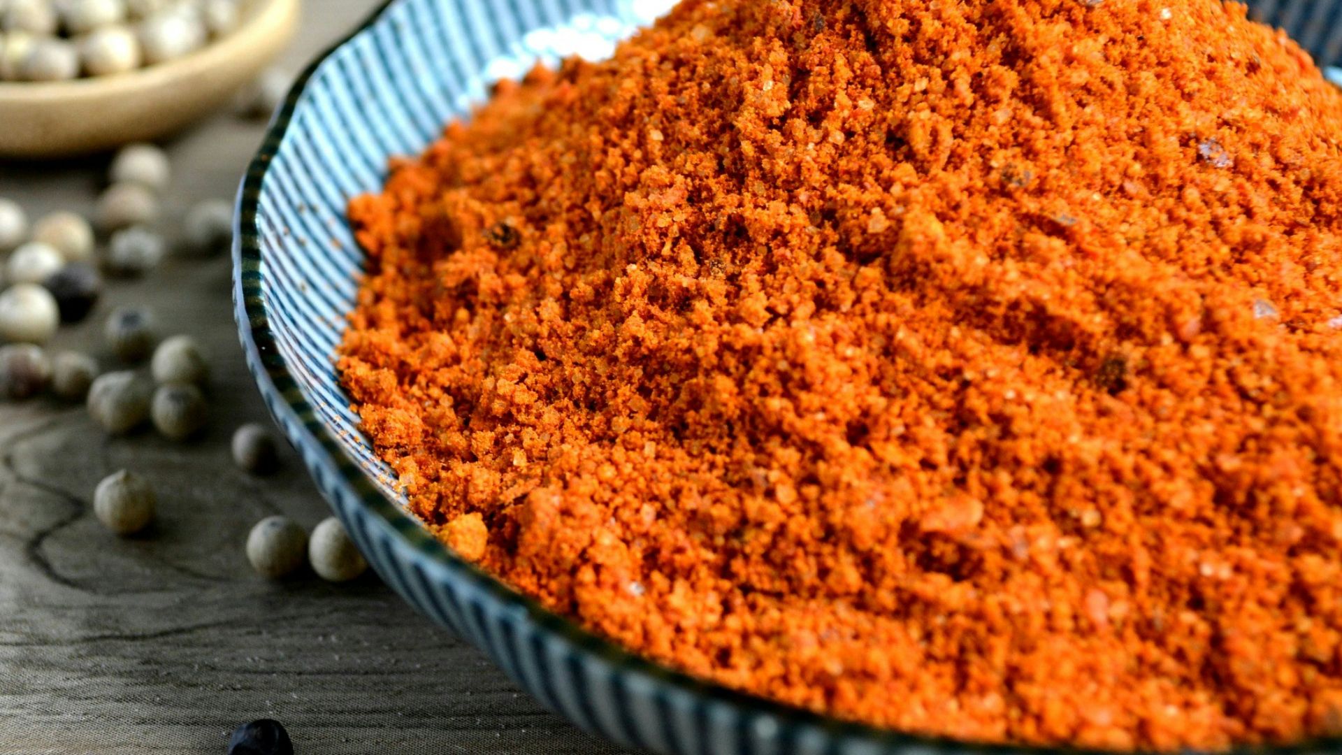 red spices on blue bowl with peppers scattered on table