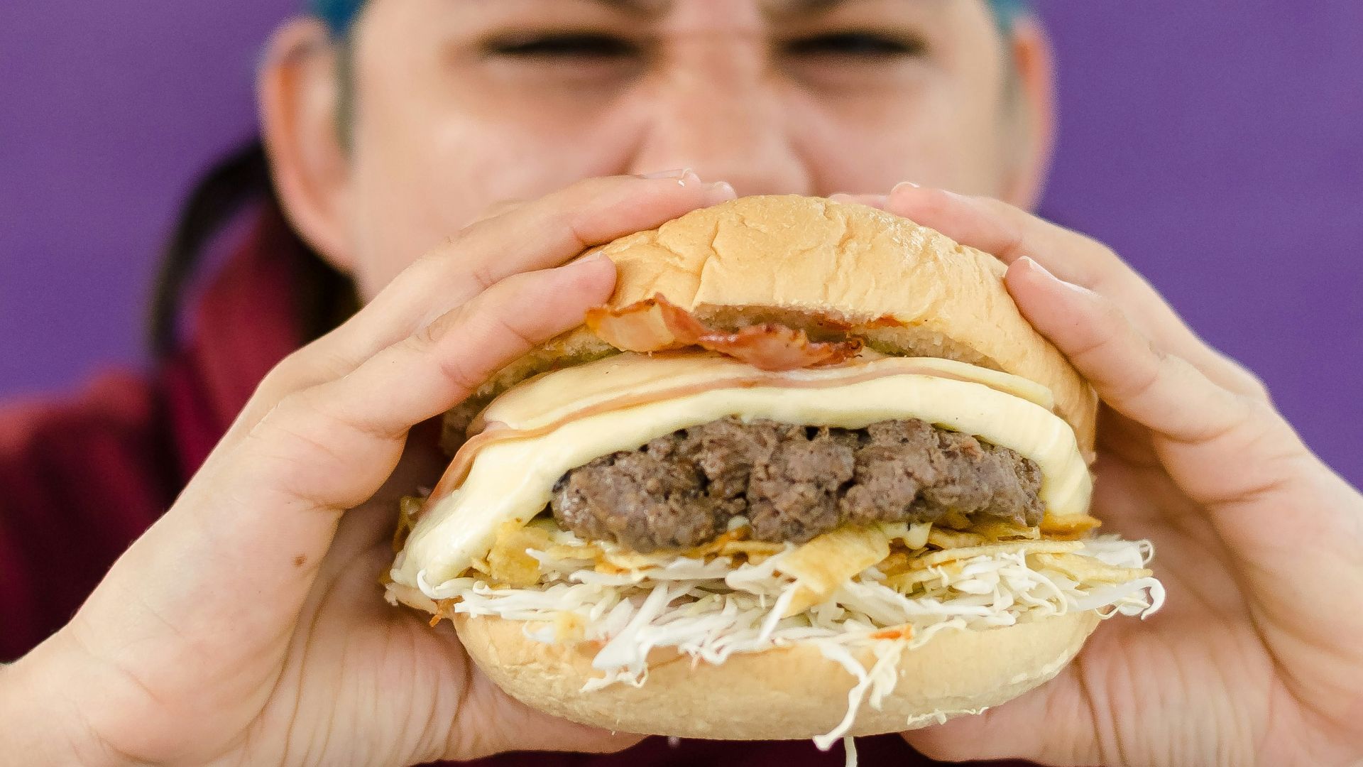 person holding burger with patty and cheese
