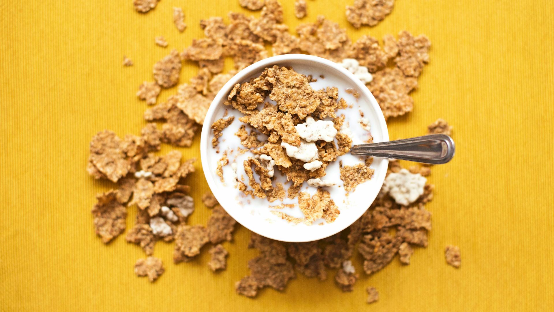 top view of corn flakes in bowl with milk and silver spoon