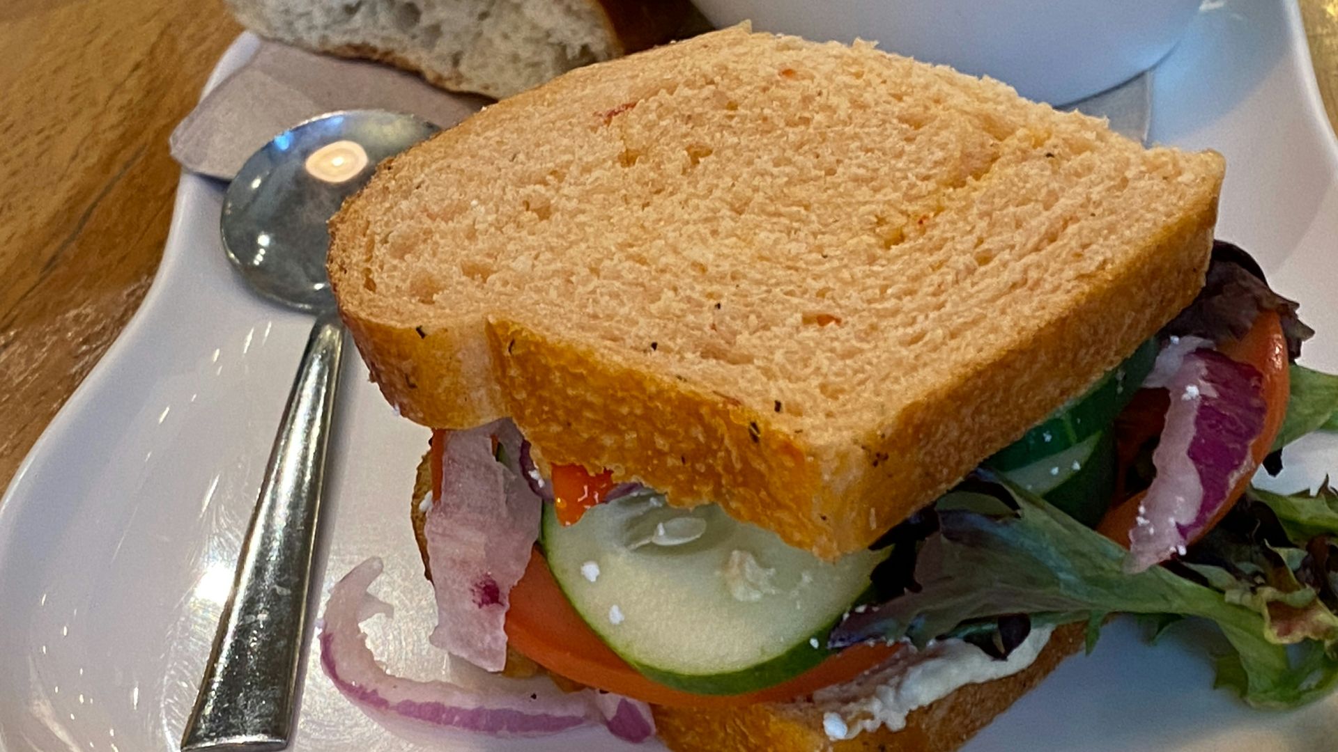 A white plate topped with a sandwich and a bowl of soup