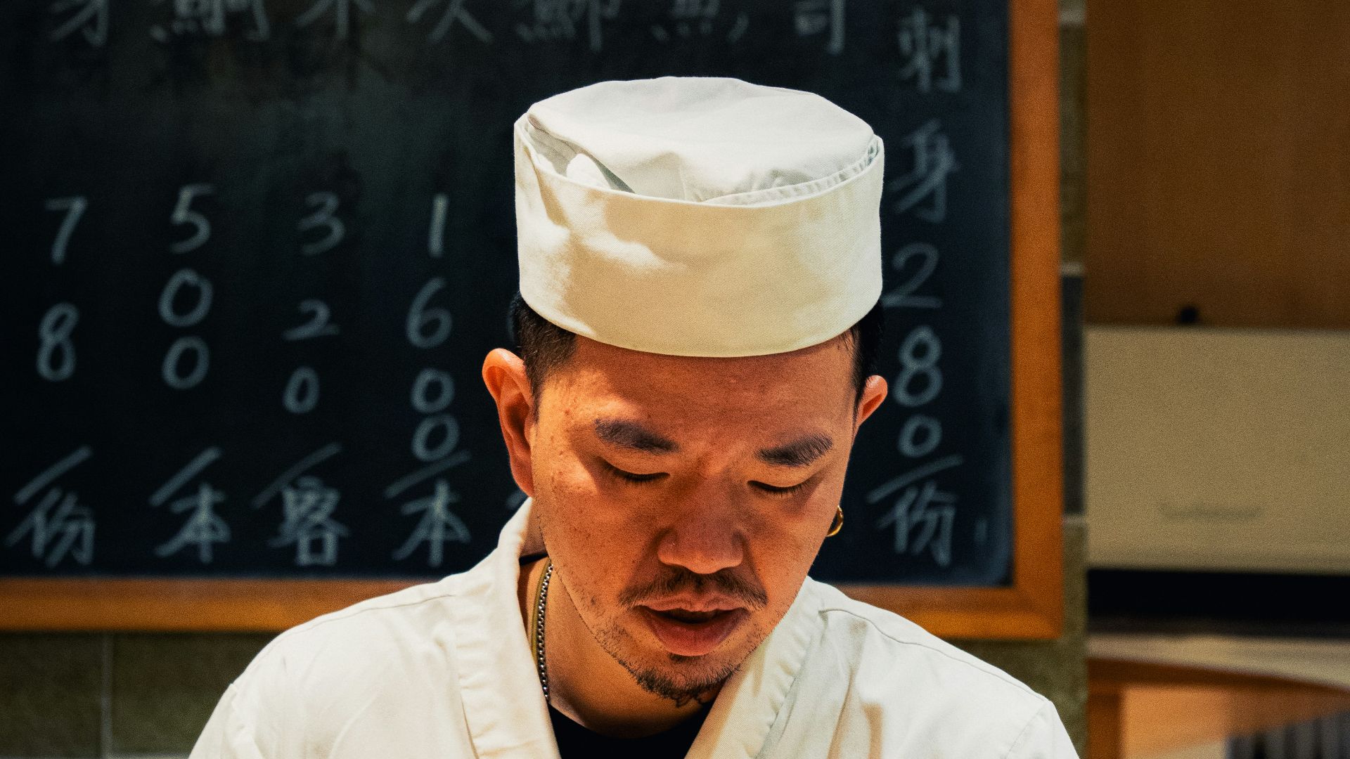 a man in a chef's outfit standing in front of a blackboard