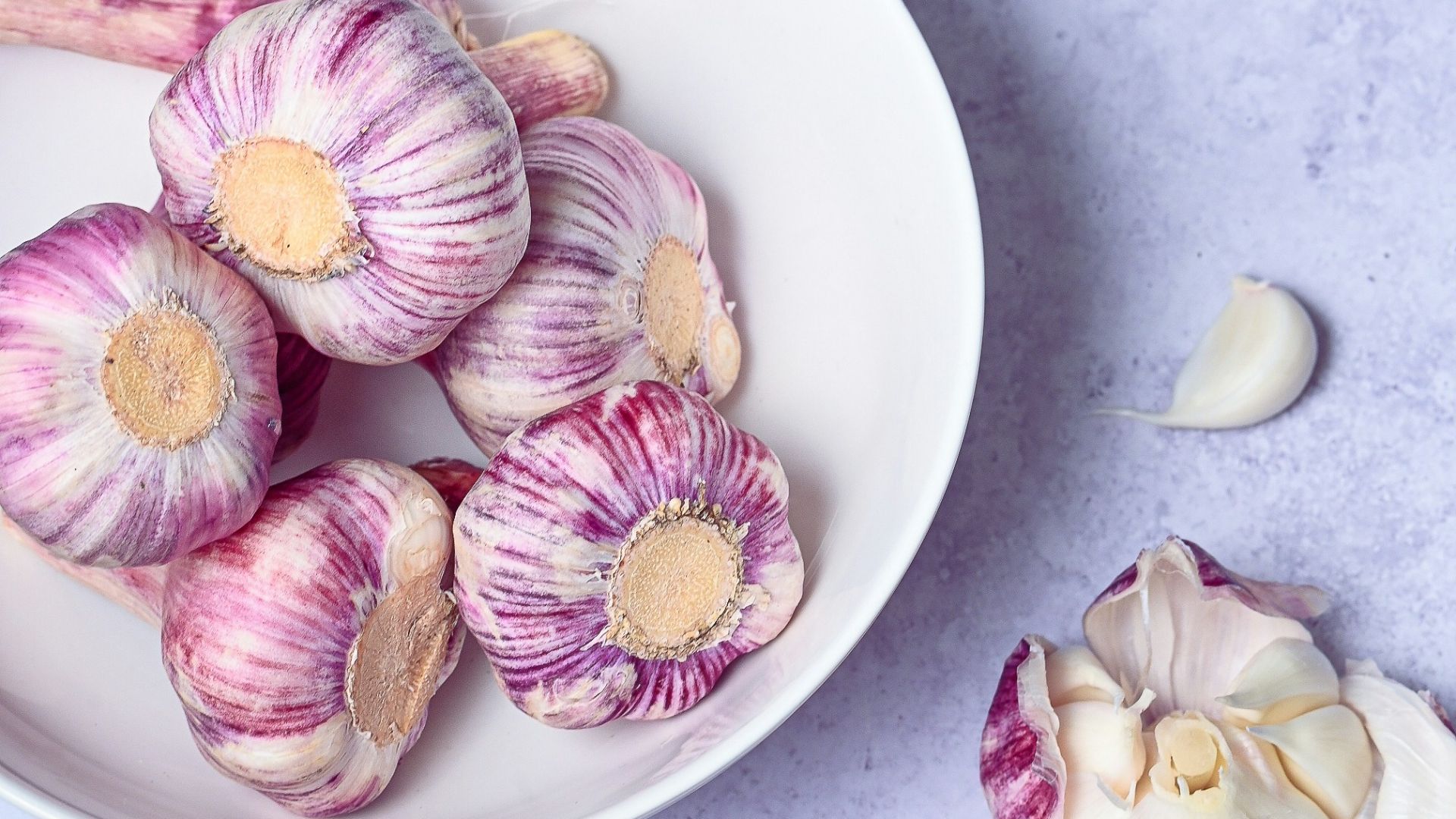 a white bowl filled with garlic next to a pile of garlic