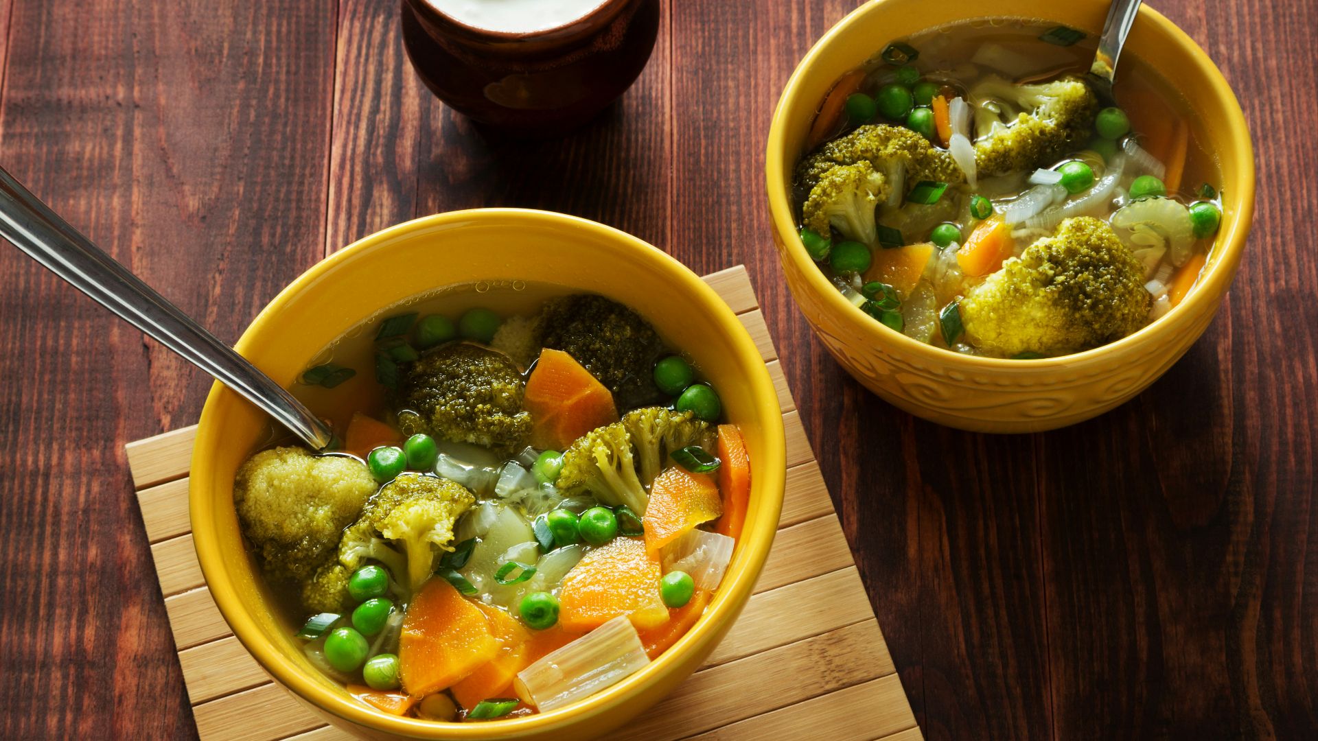 two bowls of soup with peas, carrots and broccoli