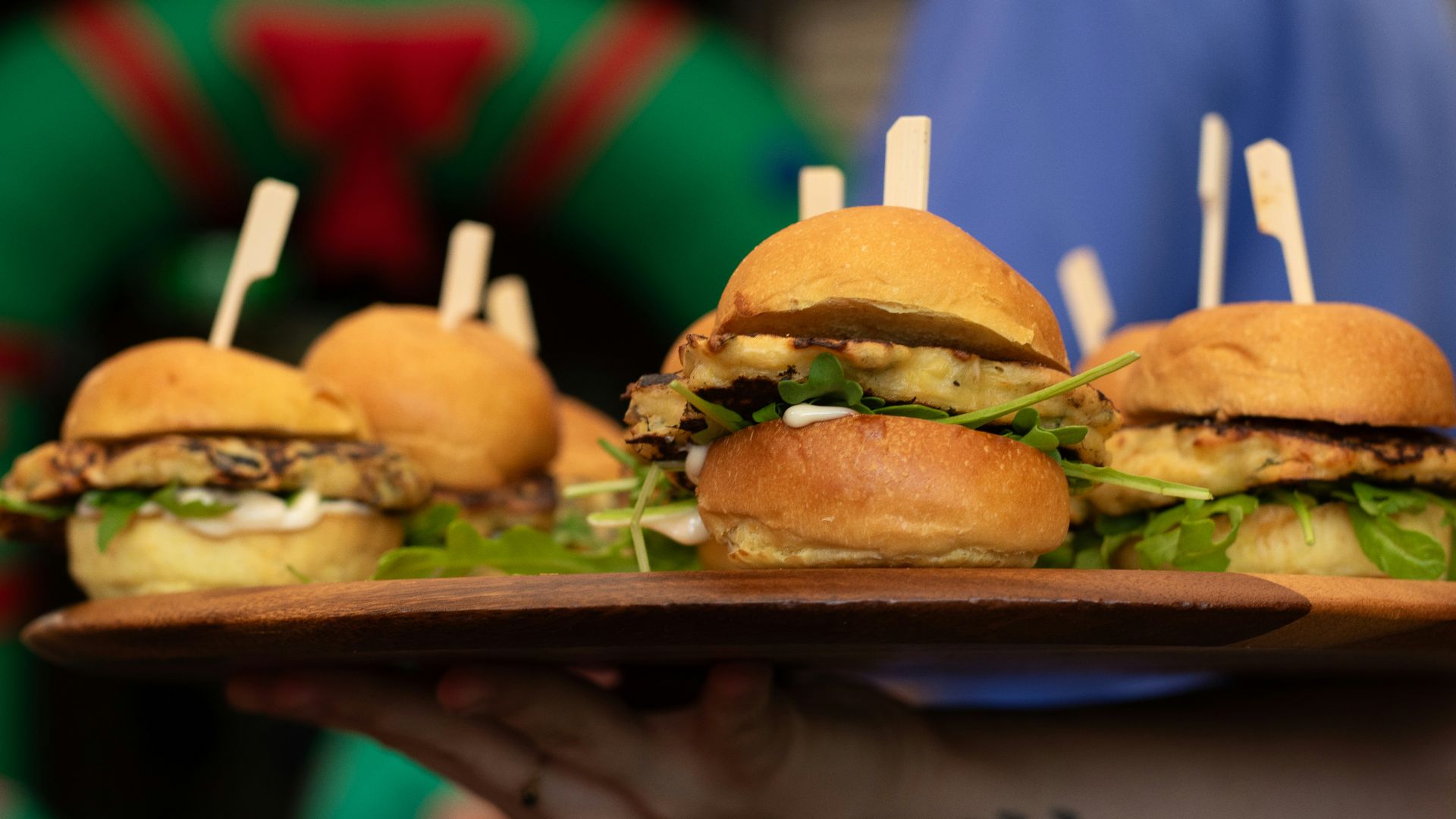 A person holding a tray of mini sandwiches