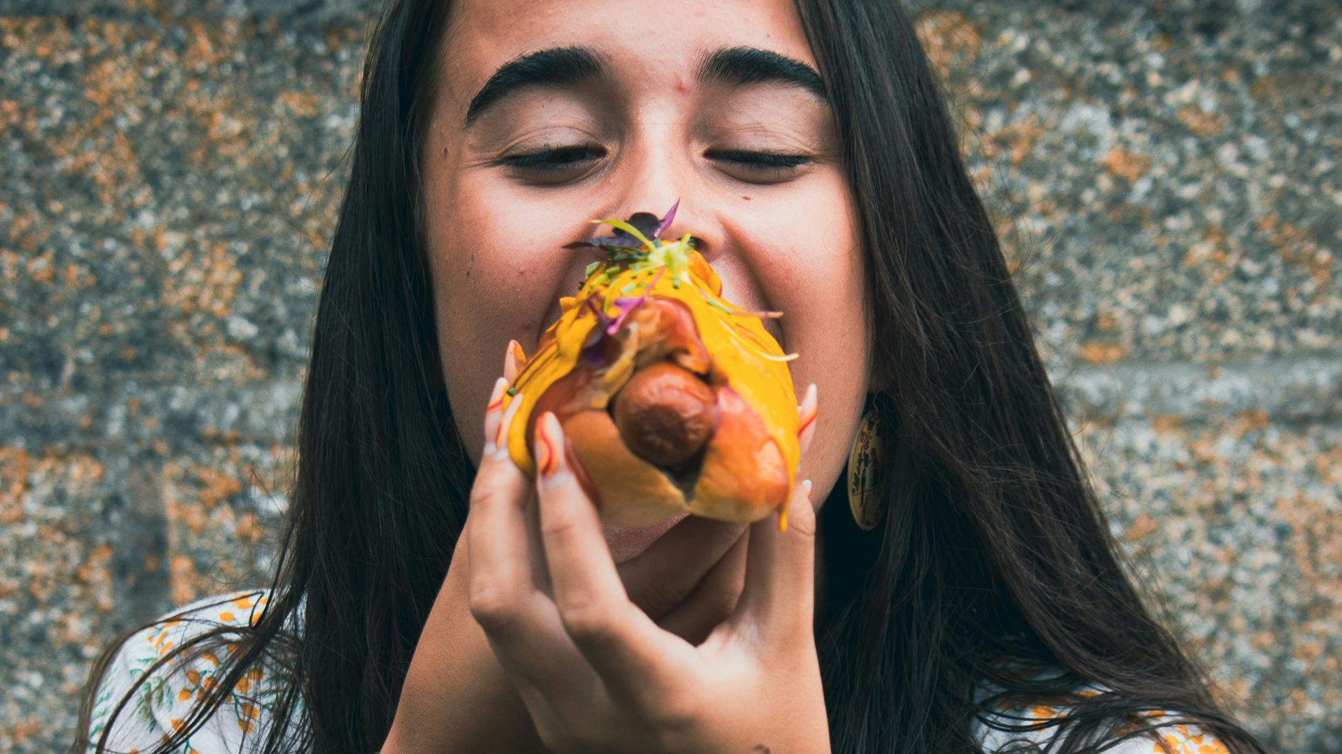 woman in white blue and red floral shirt holding a burger