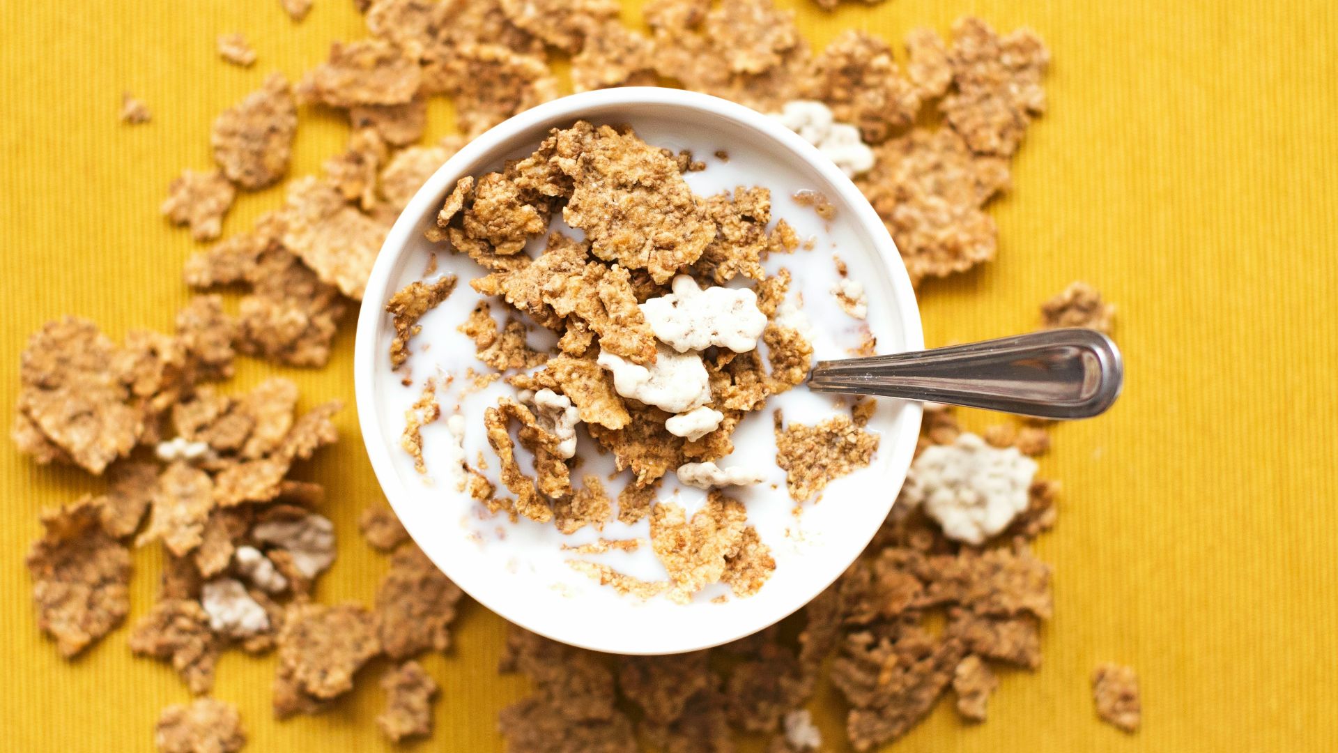 top view of corn flakes in bowl with milk and silver spoon