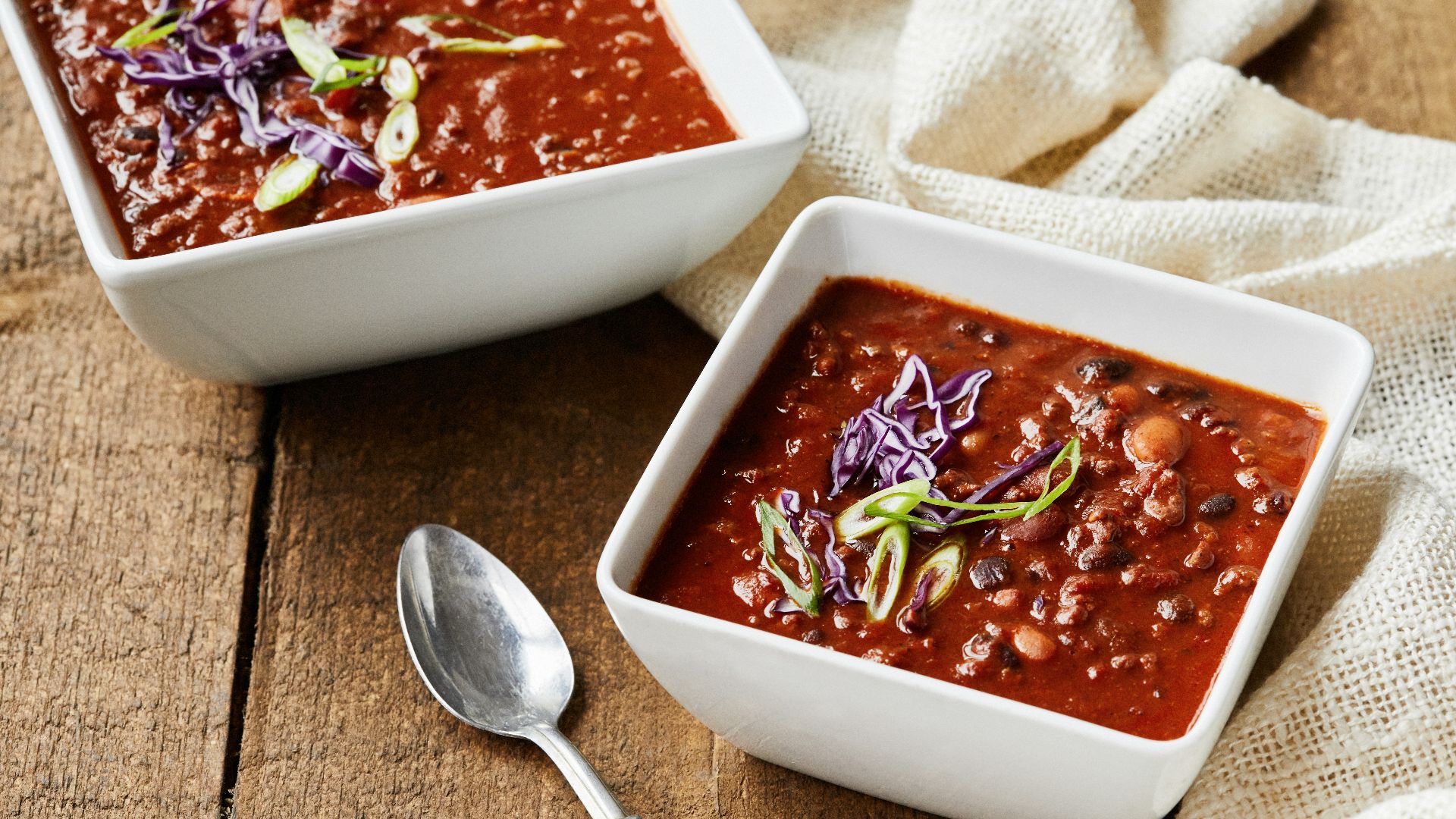 two bowls of chili and a spoon on a wooden table