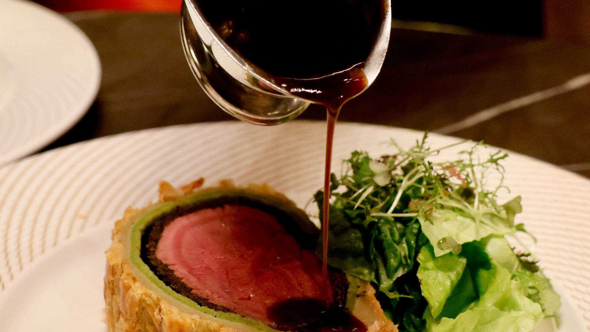 a person pouring sauce on a piece of meat