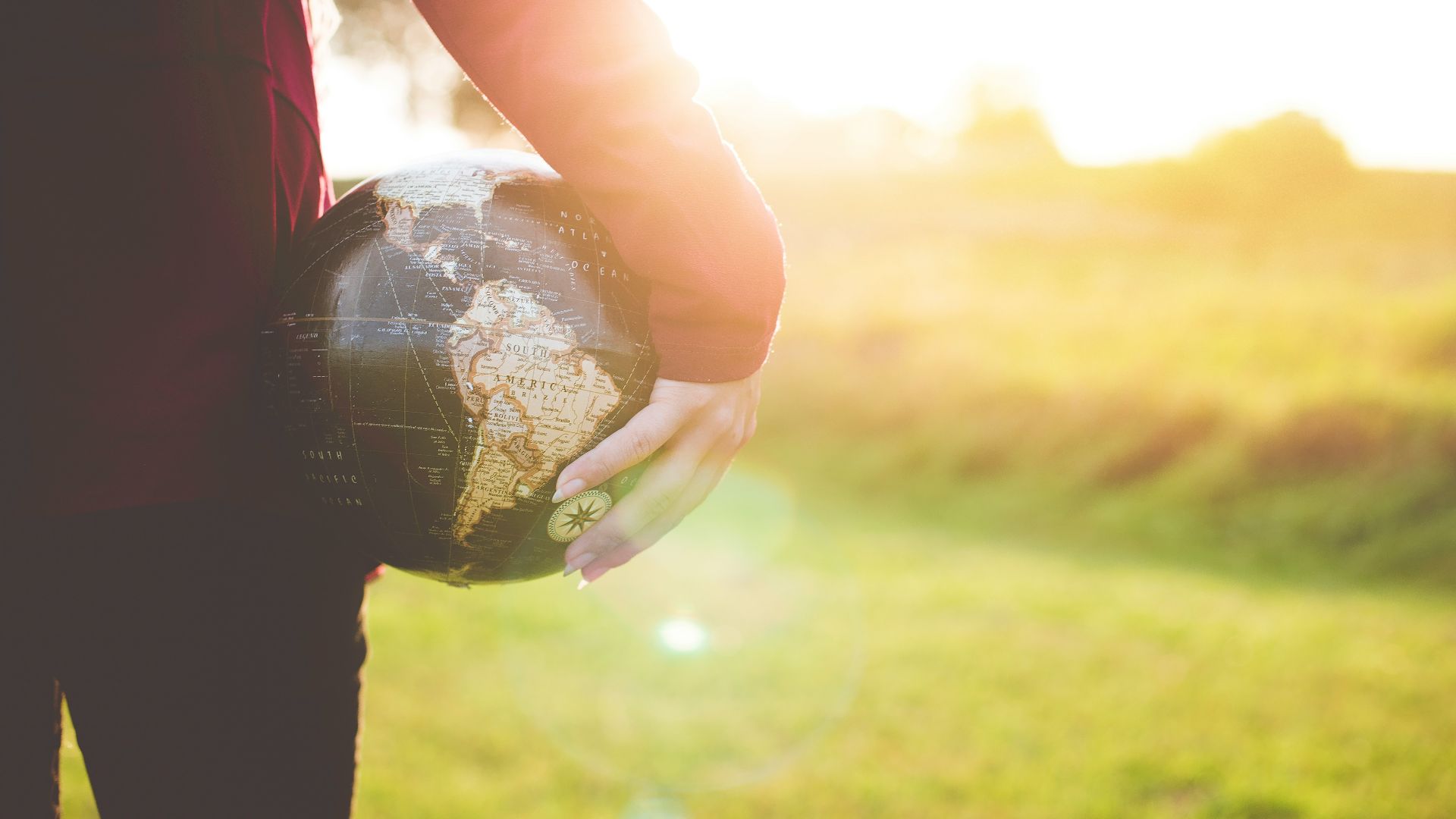 person holding black and brown globe ball while standing on grass land golden hour photography