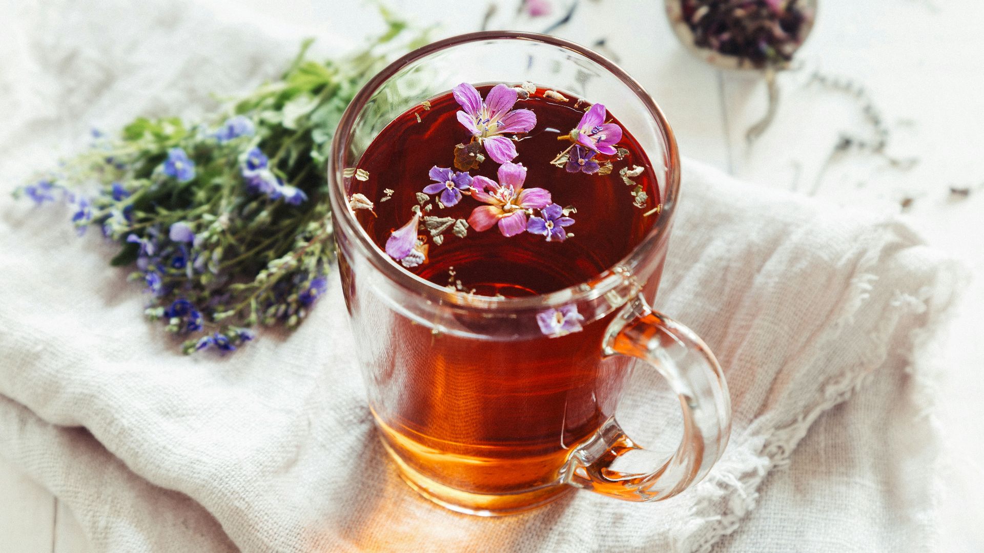 a glass mug filled with tea next to a bunch of flowers