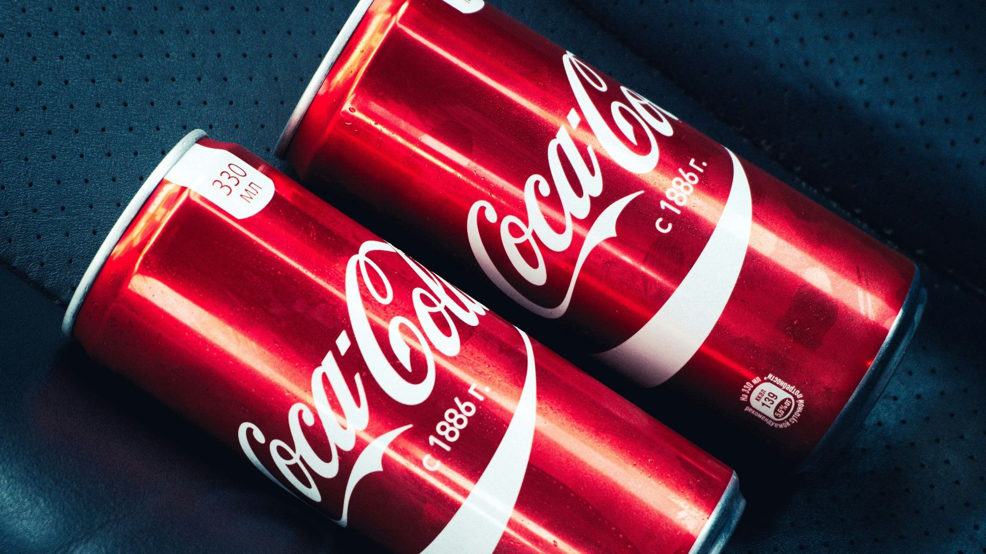 Two cans of coca - cola sitting on top of a piece of luggage