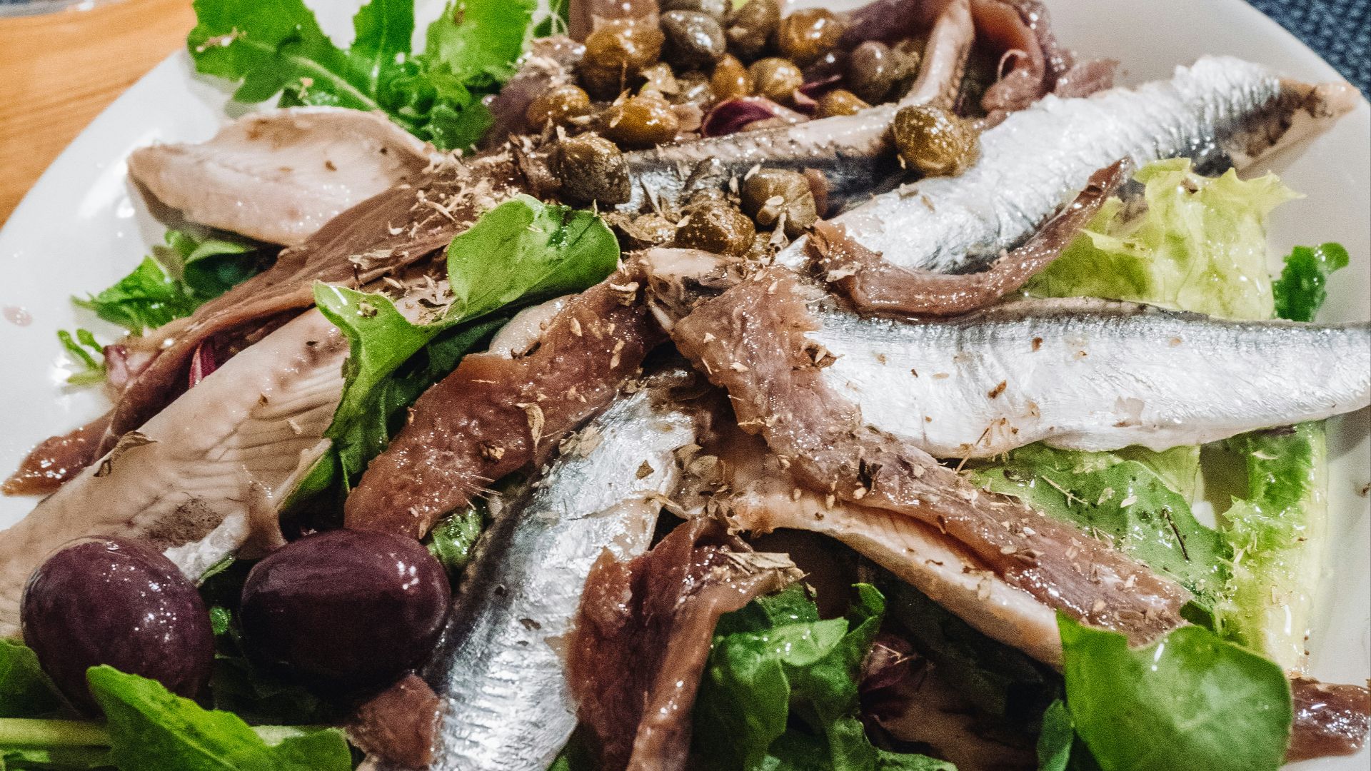 a white plate topped with a salad covered in fish