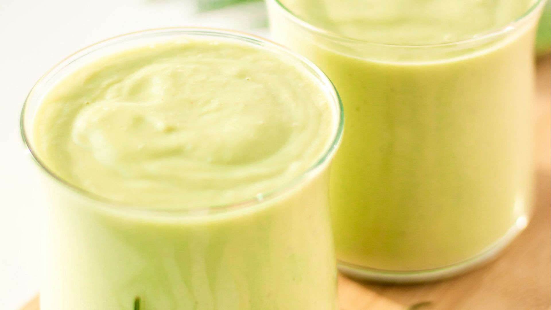 two glasses of green smoothie on a wooden tray