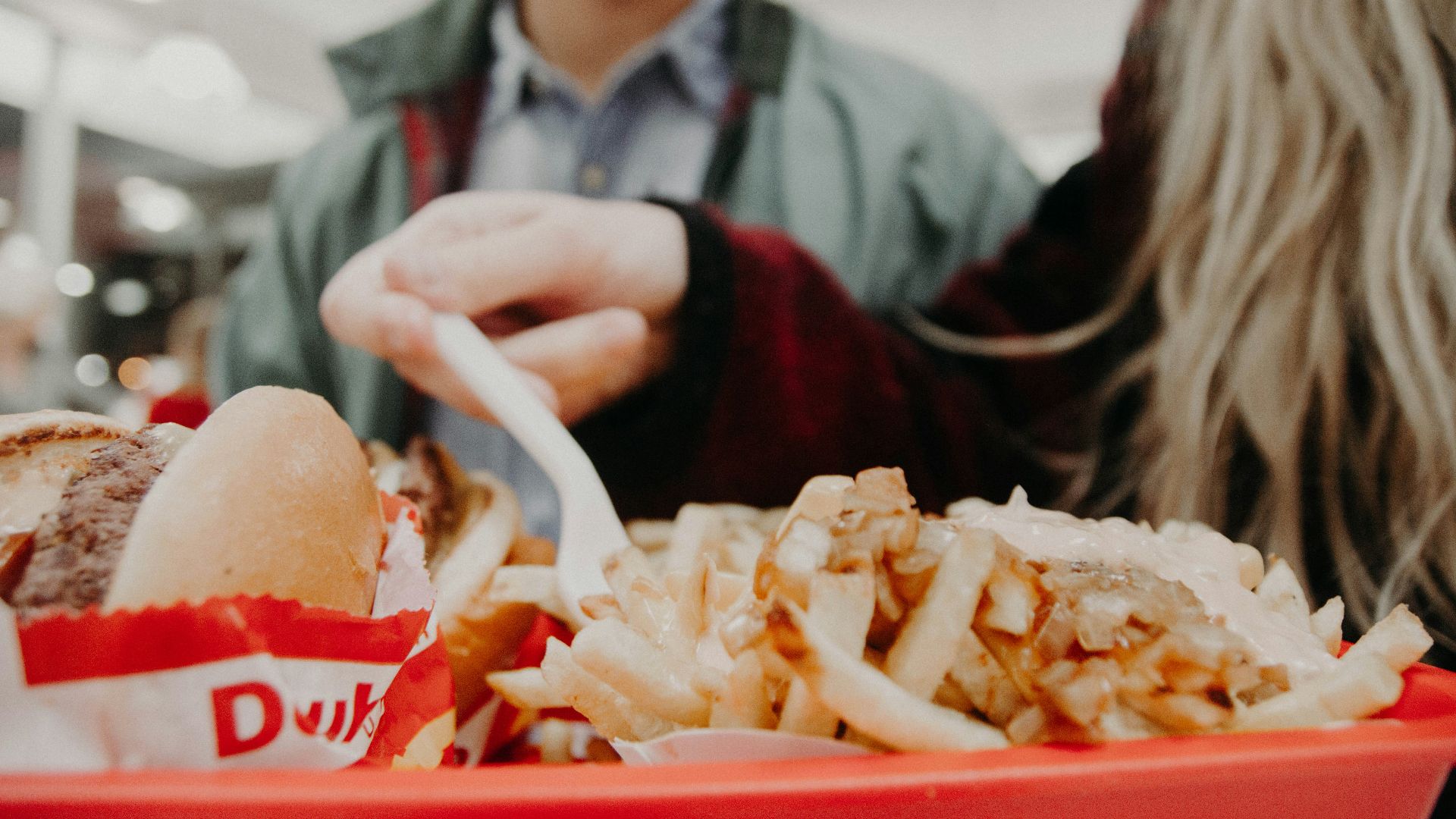 woman in maroon long-sleeved shirt holding fork over fries