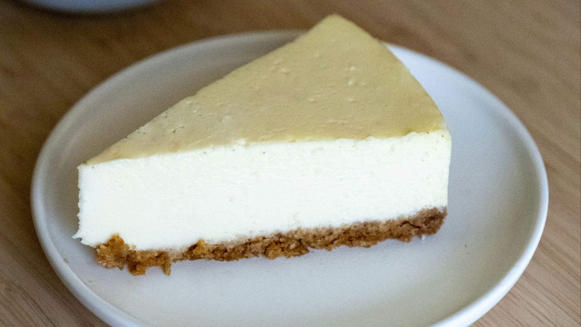 a piece of cheesecake on a plate next to a cup of tea