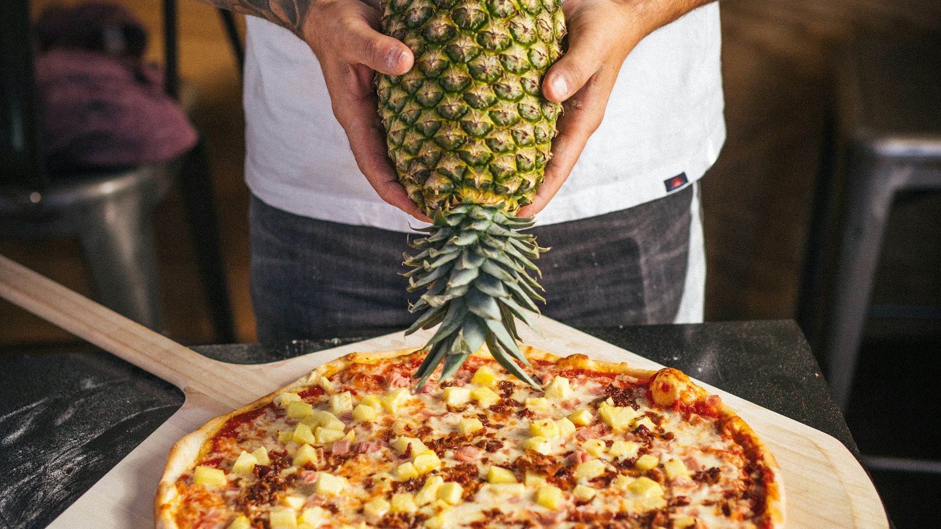 a man holding a pineapple on top of a pizza