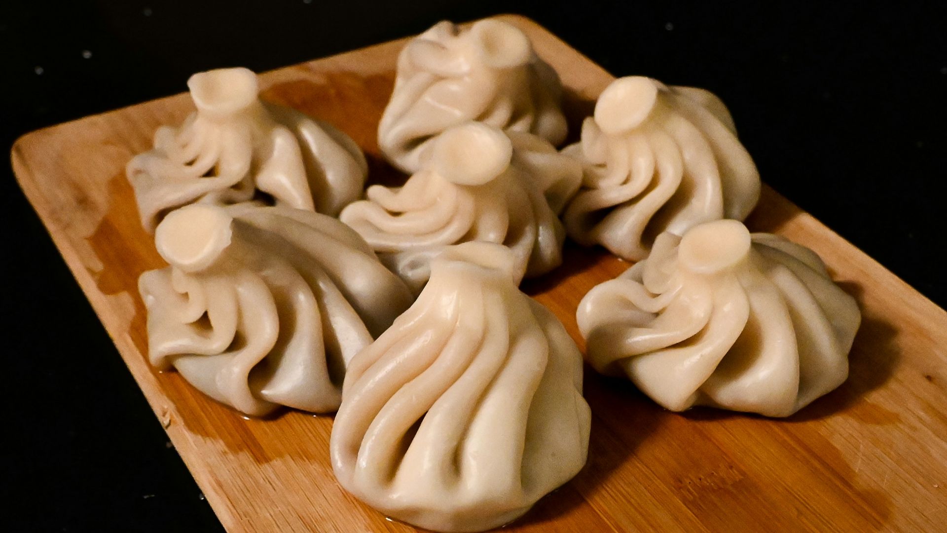 a wooden cutting board topped with dumplings on top of a table