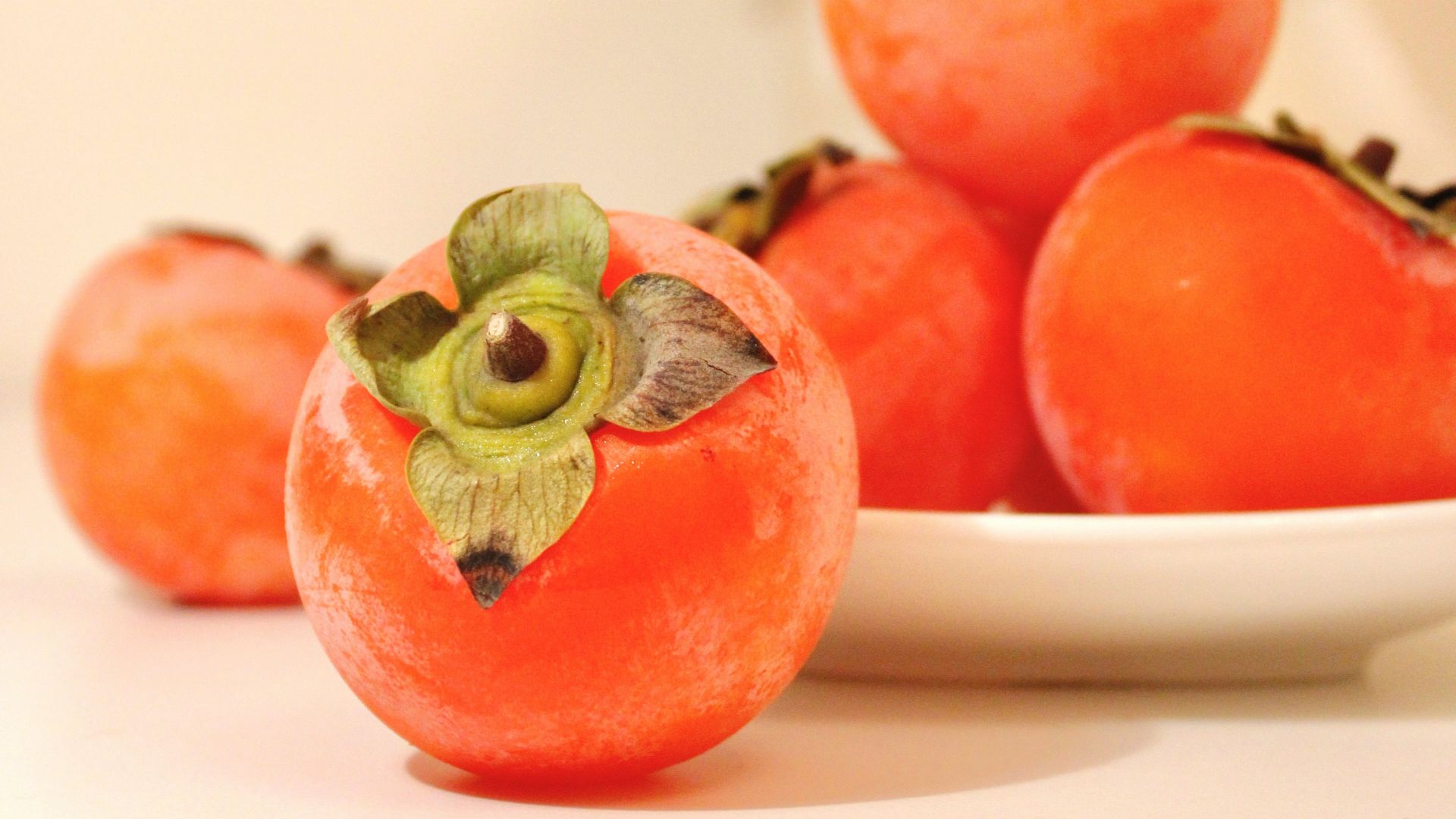 a white plate topped with tomatoes next to a vase of flowers