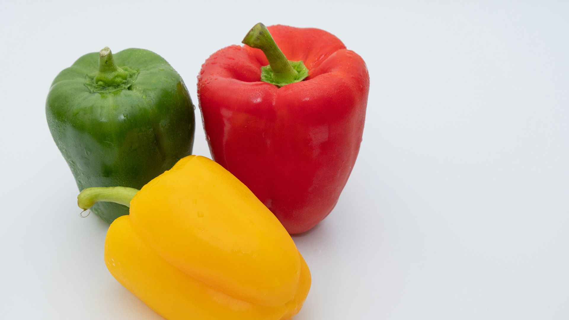 three different colored peppers on a white surface