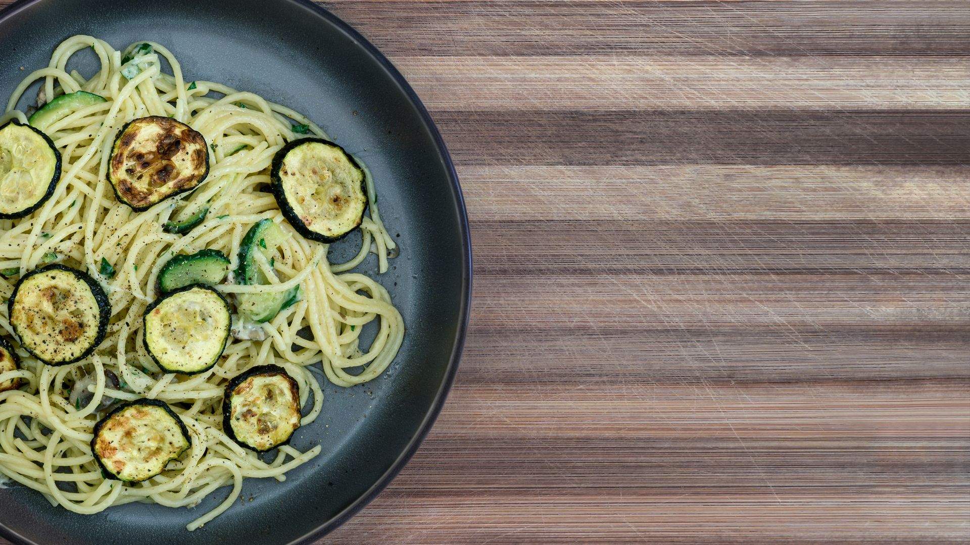 A plate of spaghetti with zucchini on a wooden table